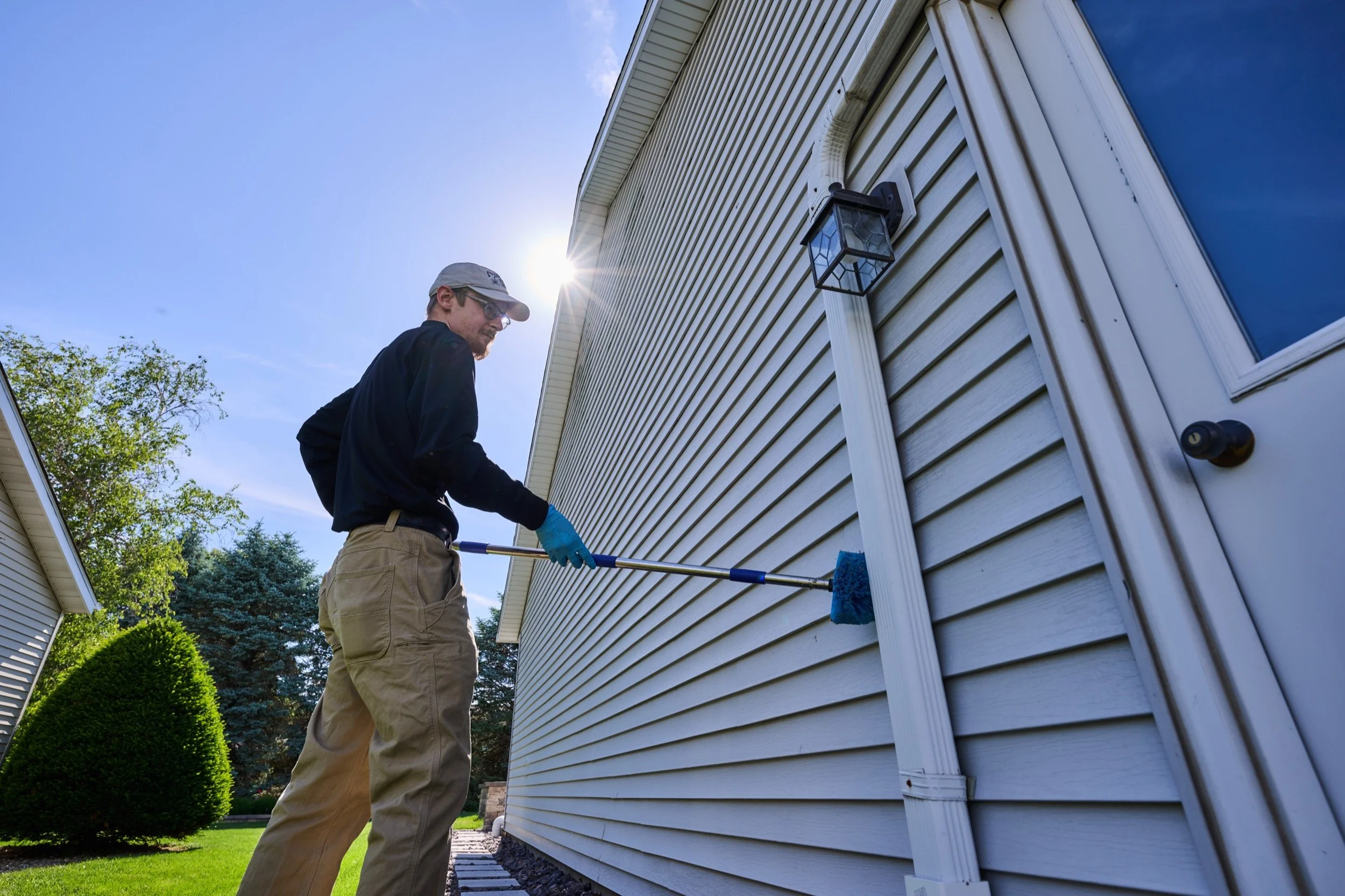 A Markley's Pest Services technician treating the sunny siding and soffit line of a Central Illinois home, where box elder bugs and lady beetles gather each fall.