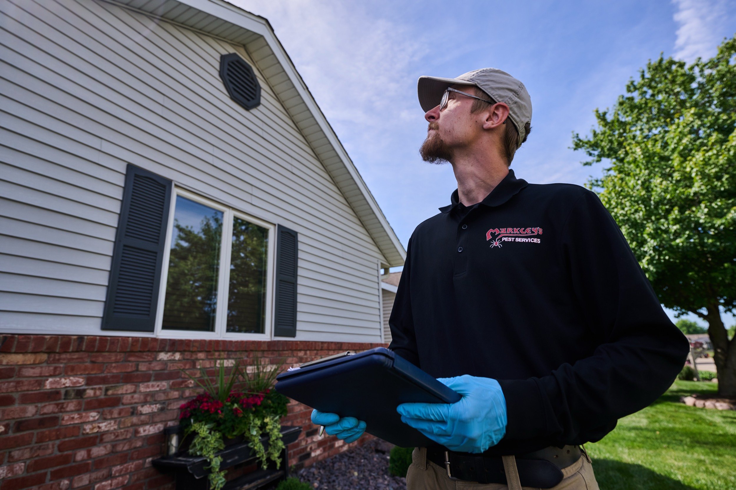 A Markley's Pest Services technician inspecting the exterior of a Central Illinois home with a tablet during a wood-damage inspection.