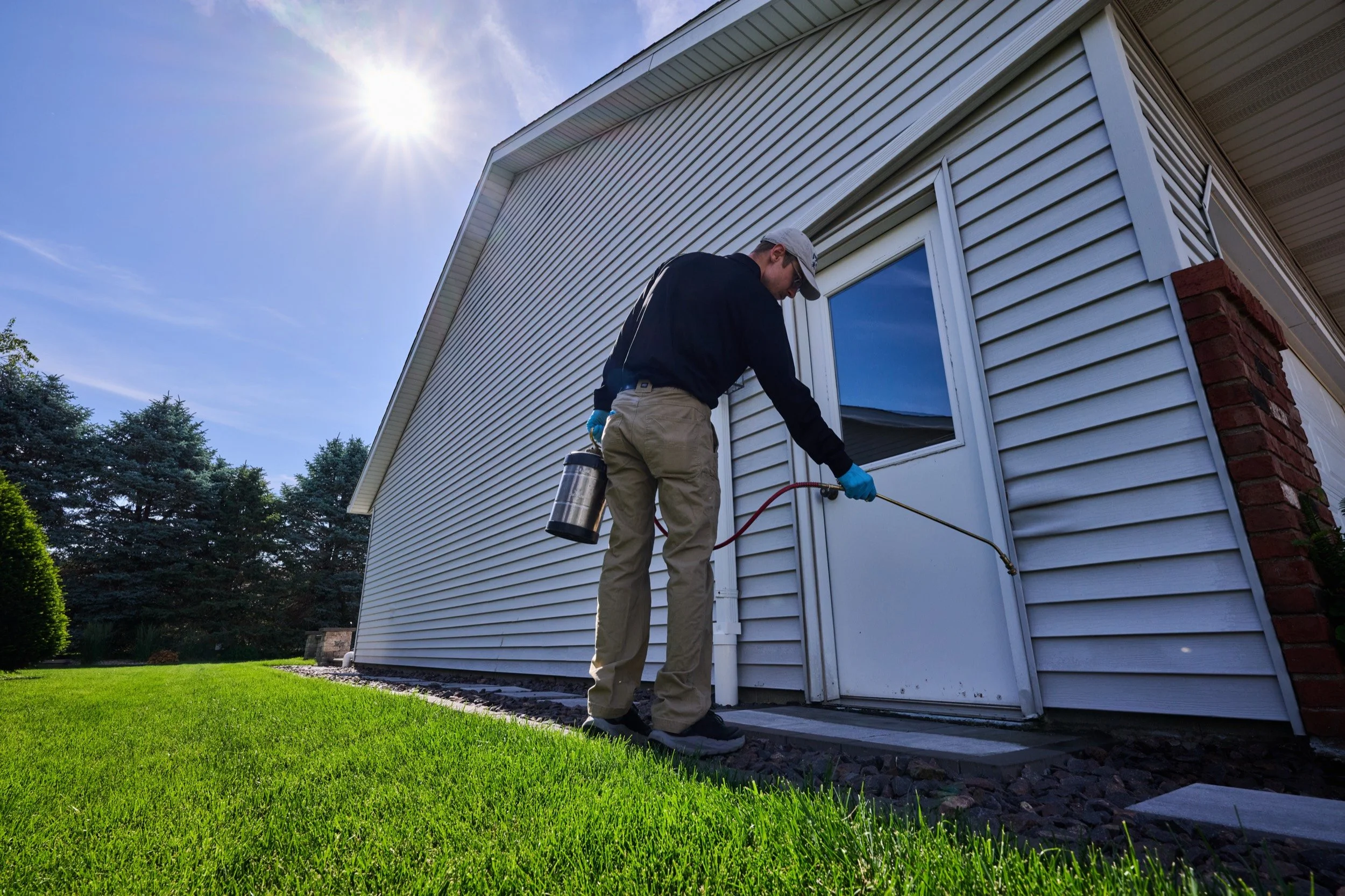 A Markley's Pest Services technician treating around the doors and windows on the sunny side of a Central Illinois home.