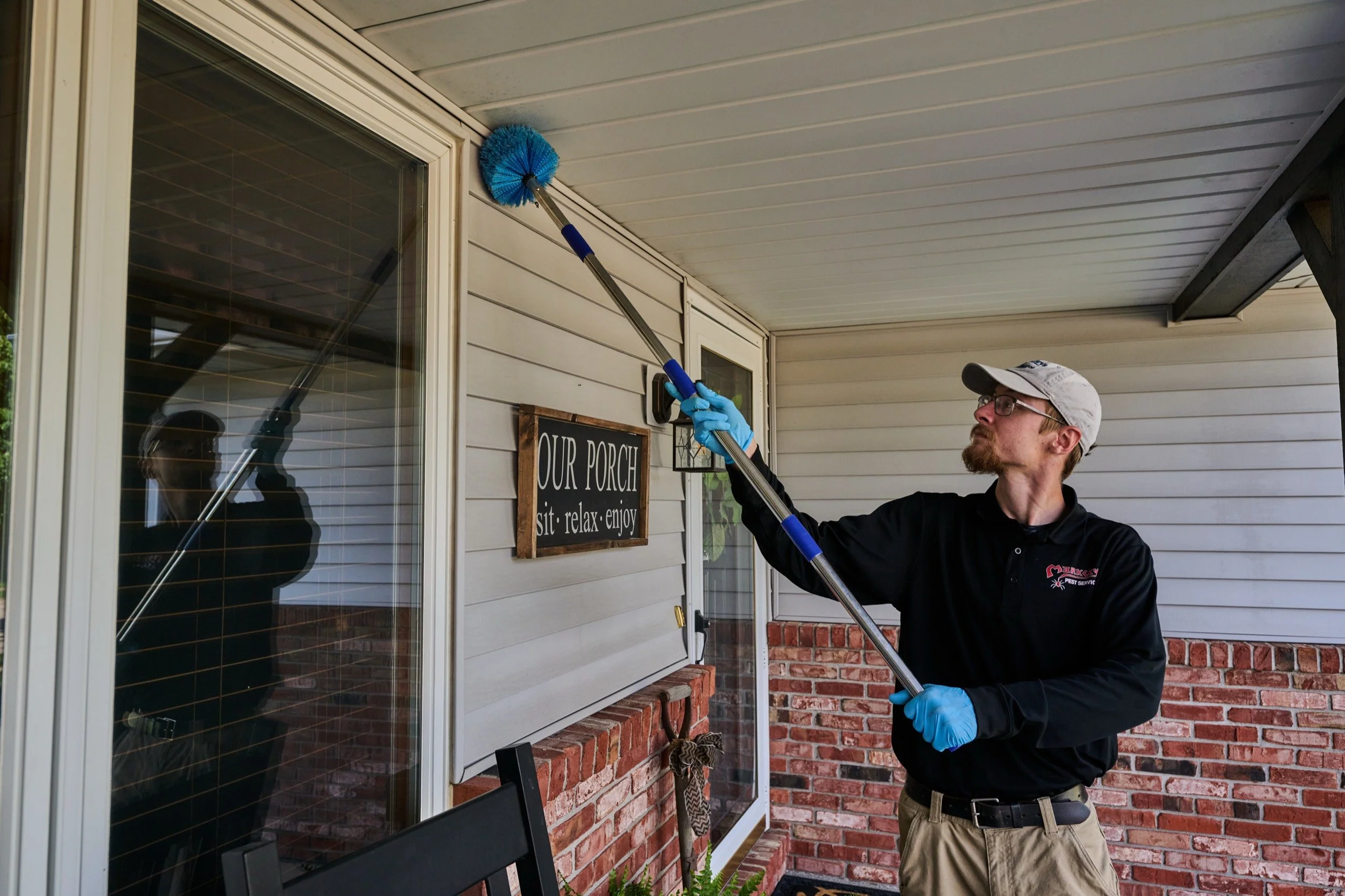 A Markley's Pest Services technician using an extension pole to clear and treat the porch ceiling of a Central Illinois home, where spider webs collect.