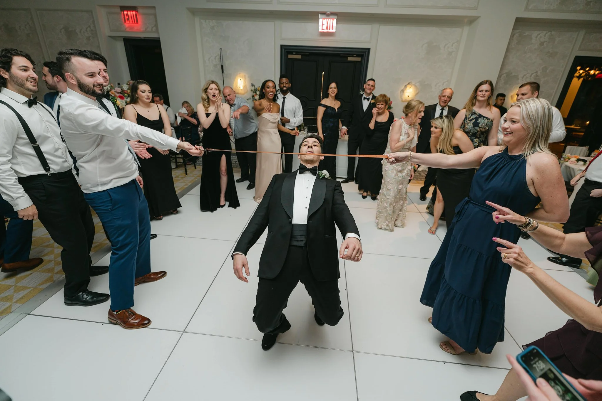 Groom going under a limbo stick at a New York City wedding reception, surrounded by guests dancing to DJ Xenia’s music