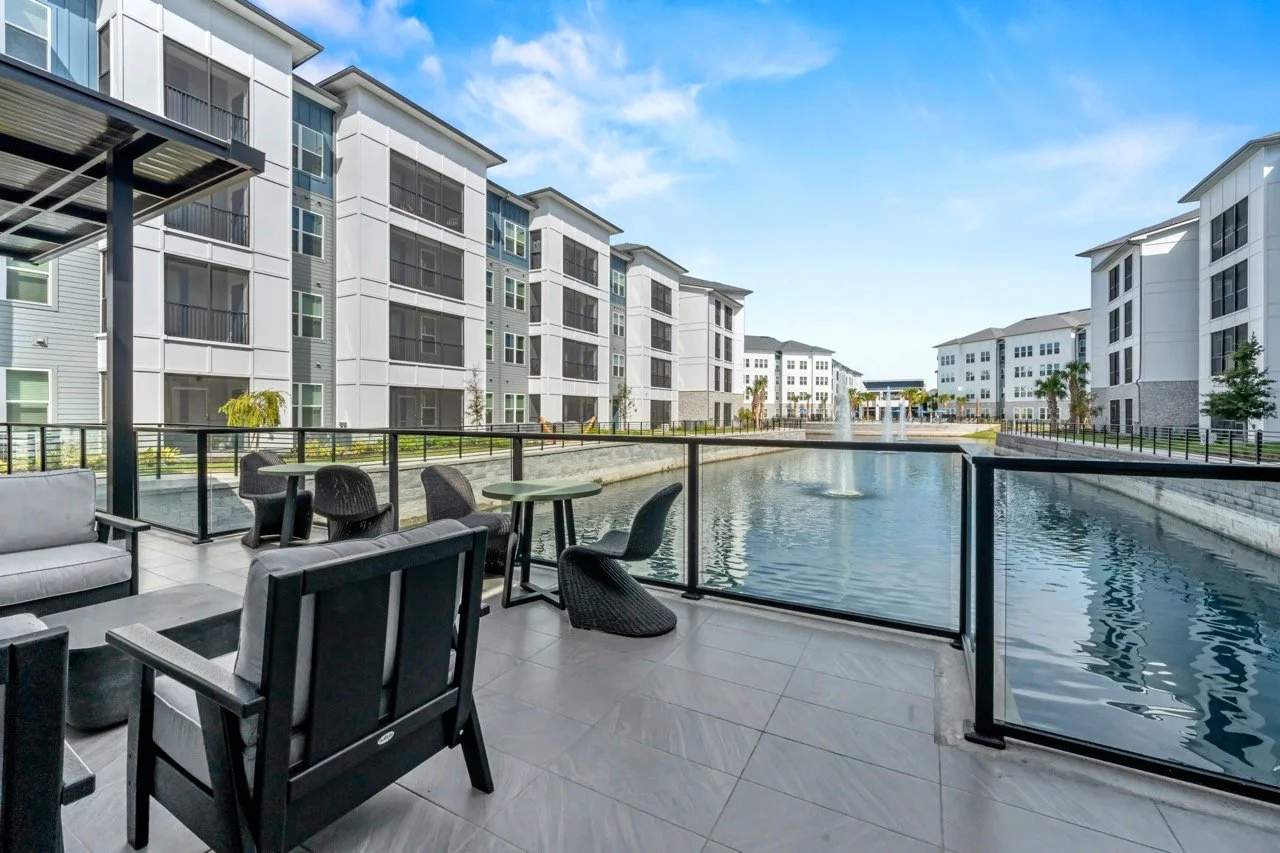 Balcony with outdoor seating overlooking a water feature in a modern apartment complex.