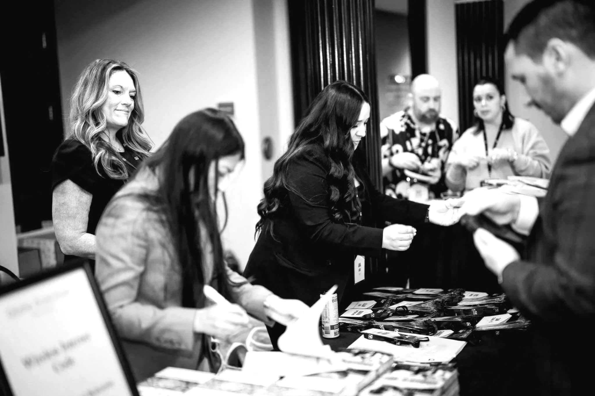 People attending a registration or check-in table at an event, with staff handing out materials and using a laptop.