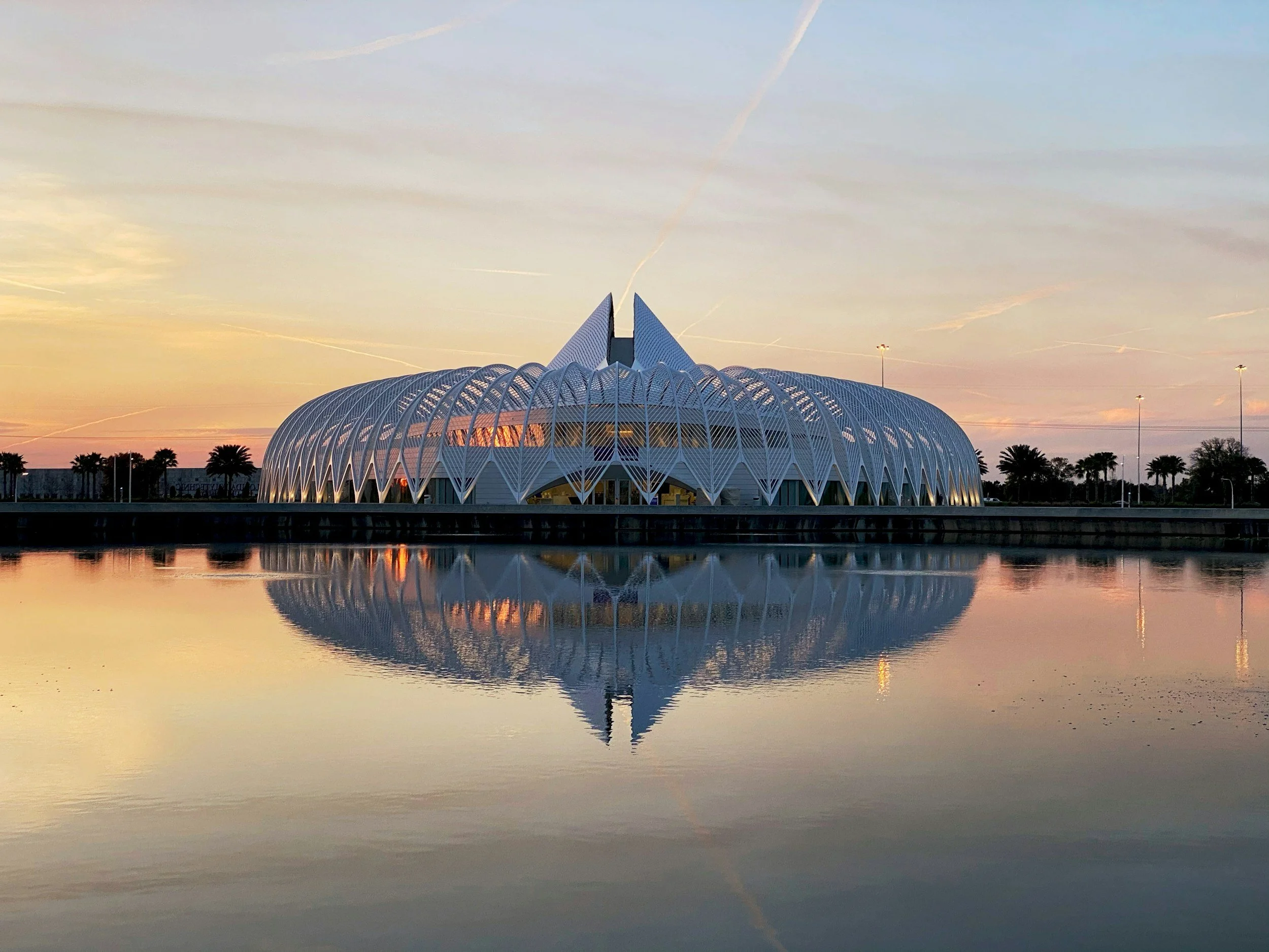 Modern art museum with a unique, futuristic design reflected in a body of water during sunset.