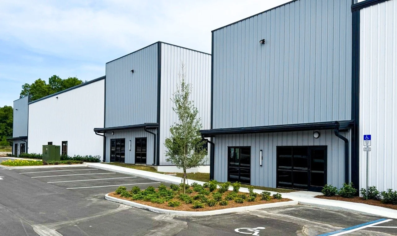Modern industrial building with a parking lot, including a handicapped parking space, and small landscaped trees and bushes.