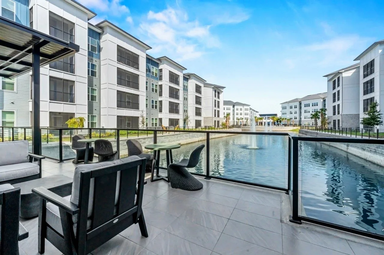 Balcony with outdoor seating overlooking a water feature in a modern apartment complex.
