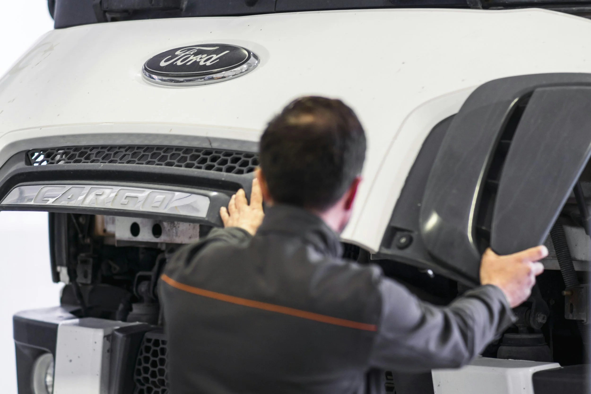 Person working on the front of a white Ford vehicle, possibly a truck or SUV, with a focus on the grille and badge.