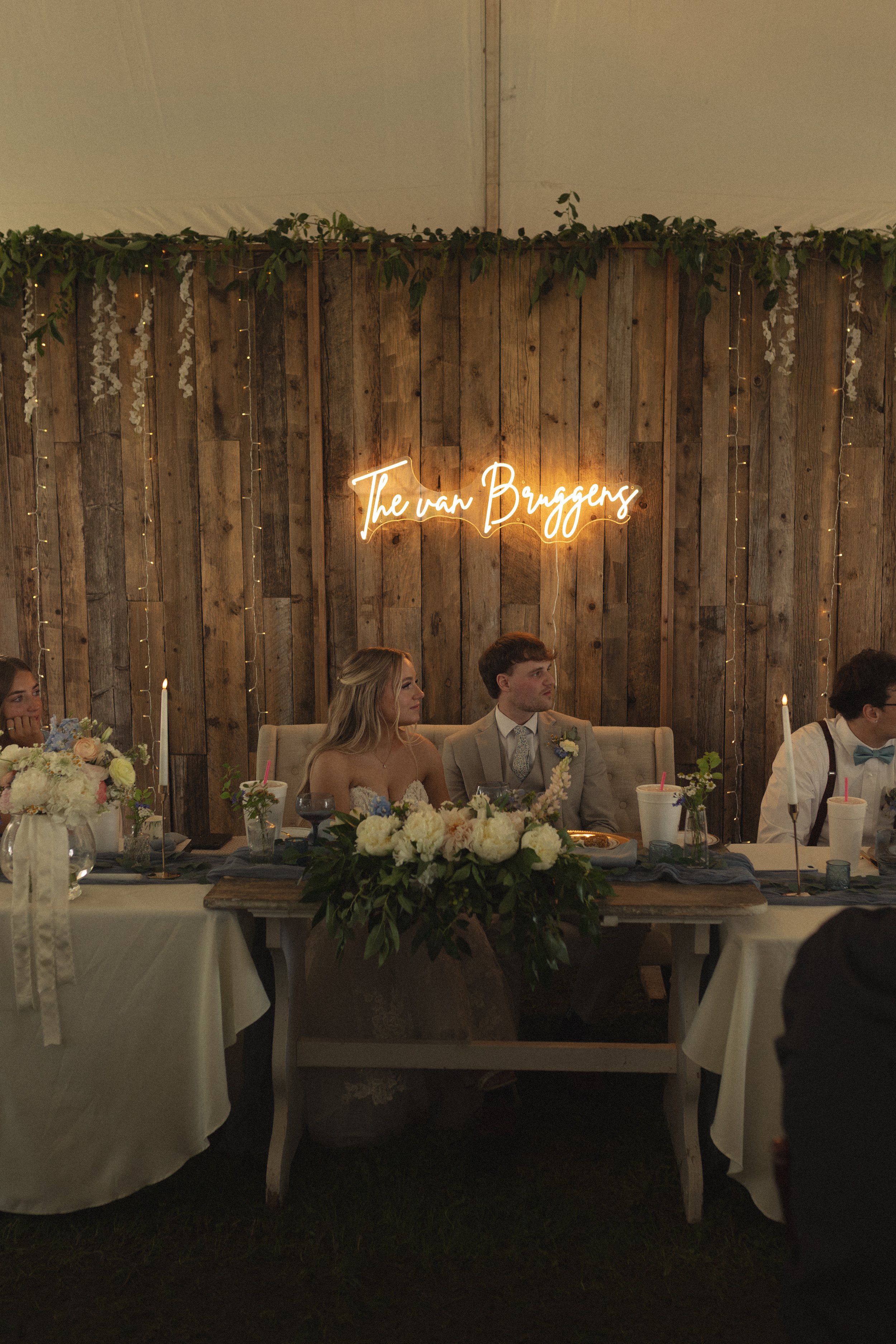A close-up of a bouquet with pink peonies, white cosmos, red and white astilbe, and green leaves, placed in a glass vase.