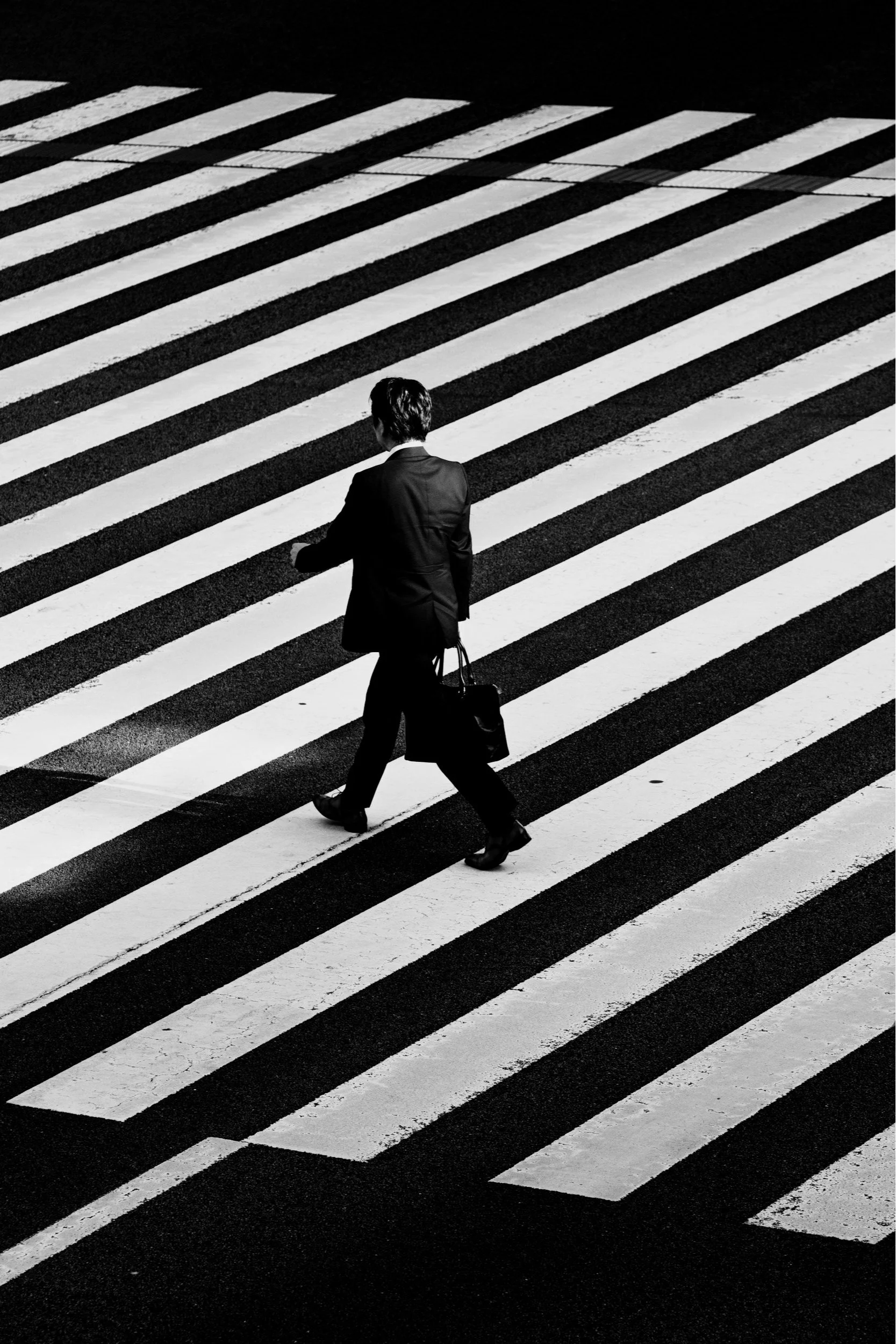 A person walking across a zebra-striped crosswalk in a city street at night, wearing a suit and carrying a briefcase.