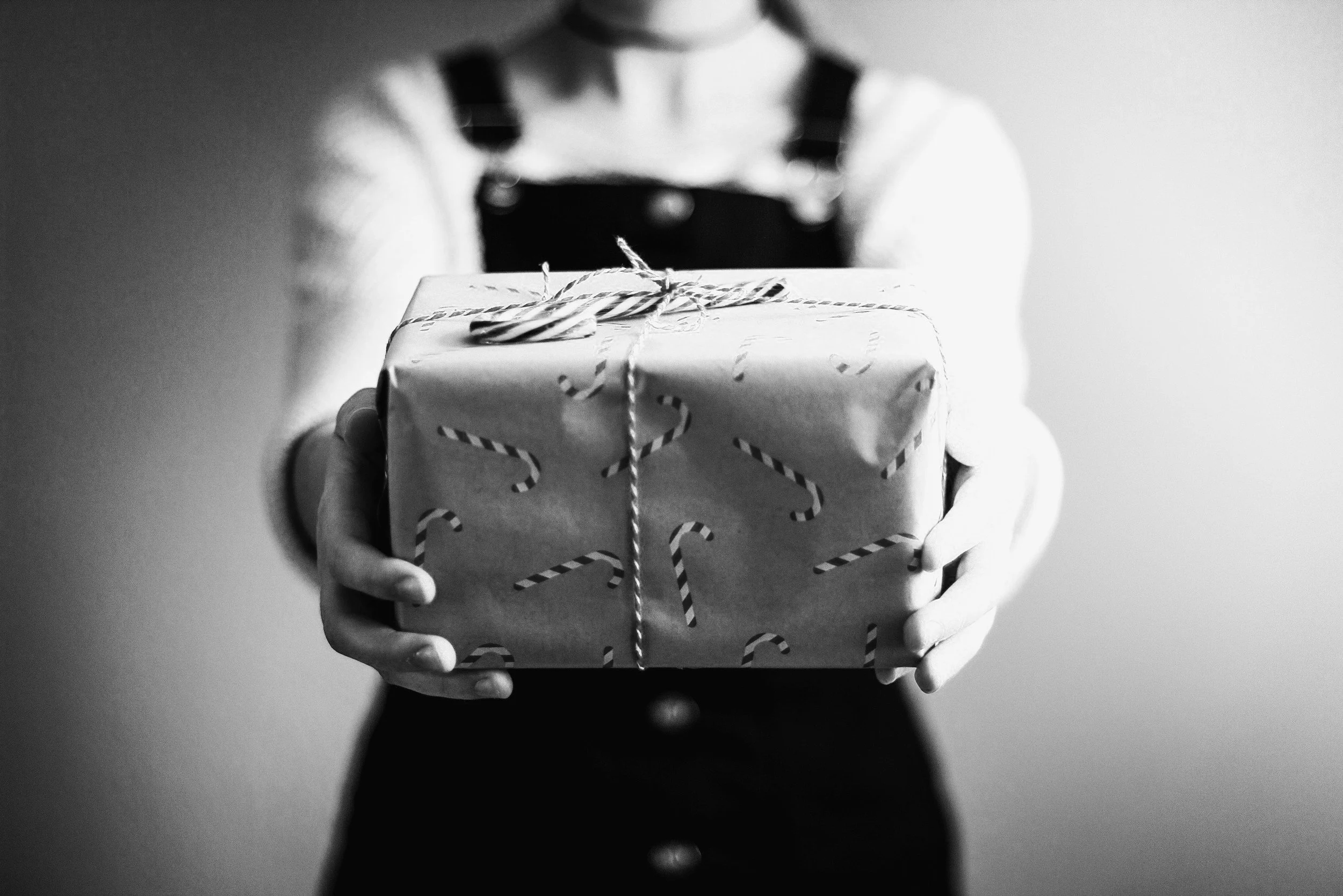 Person holding wrapped gift with candy cane pattern on the wrapping paper, black-and-white photo.