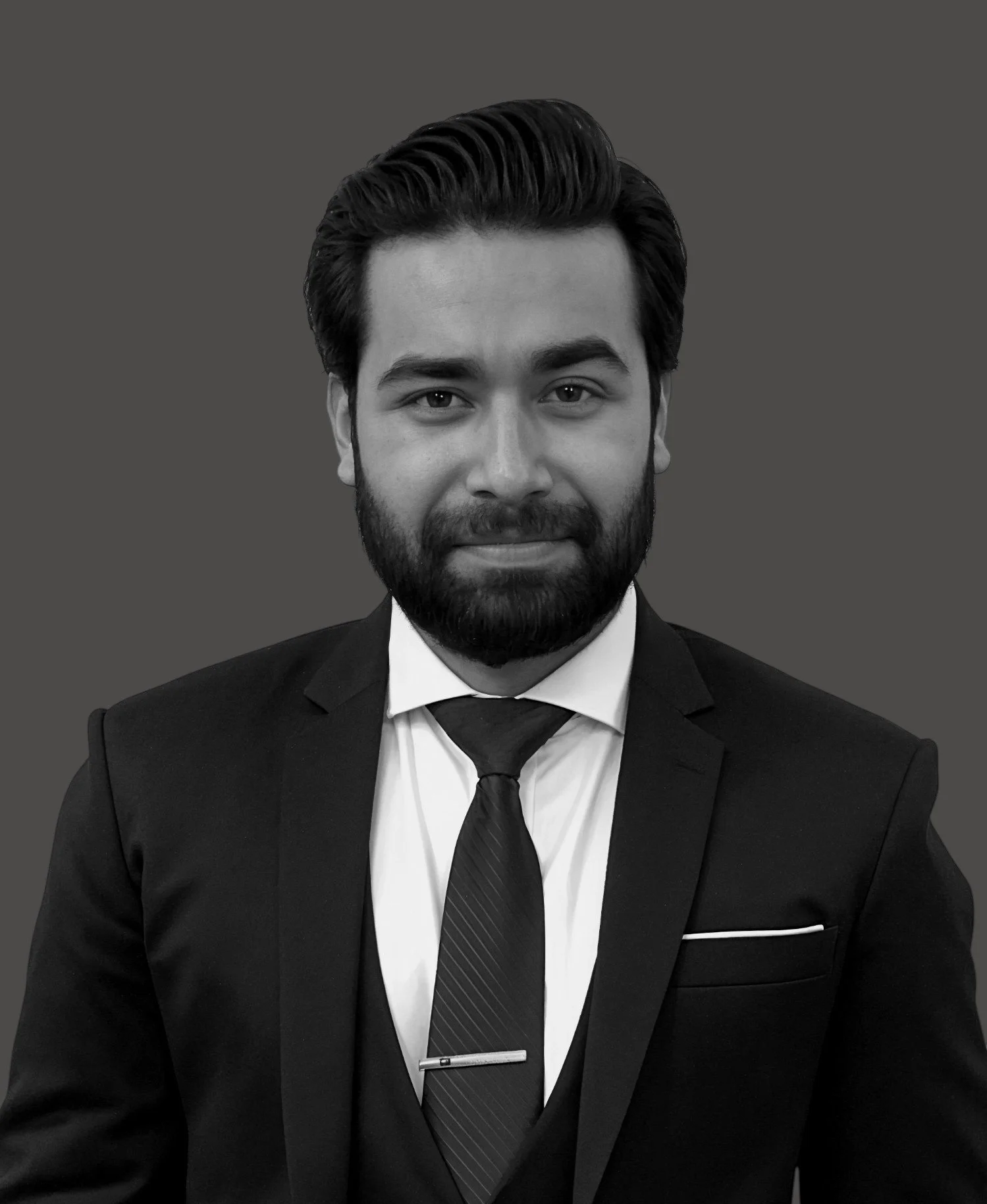 Black and white professional headshot of a man with dark hair, beard, dressed in a suit and tie, against a plain background.