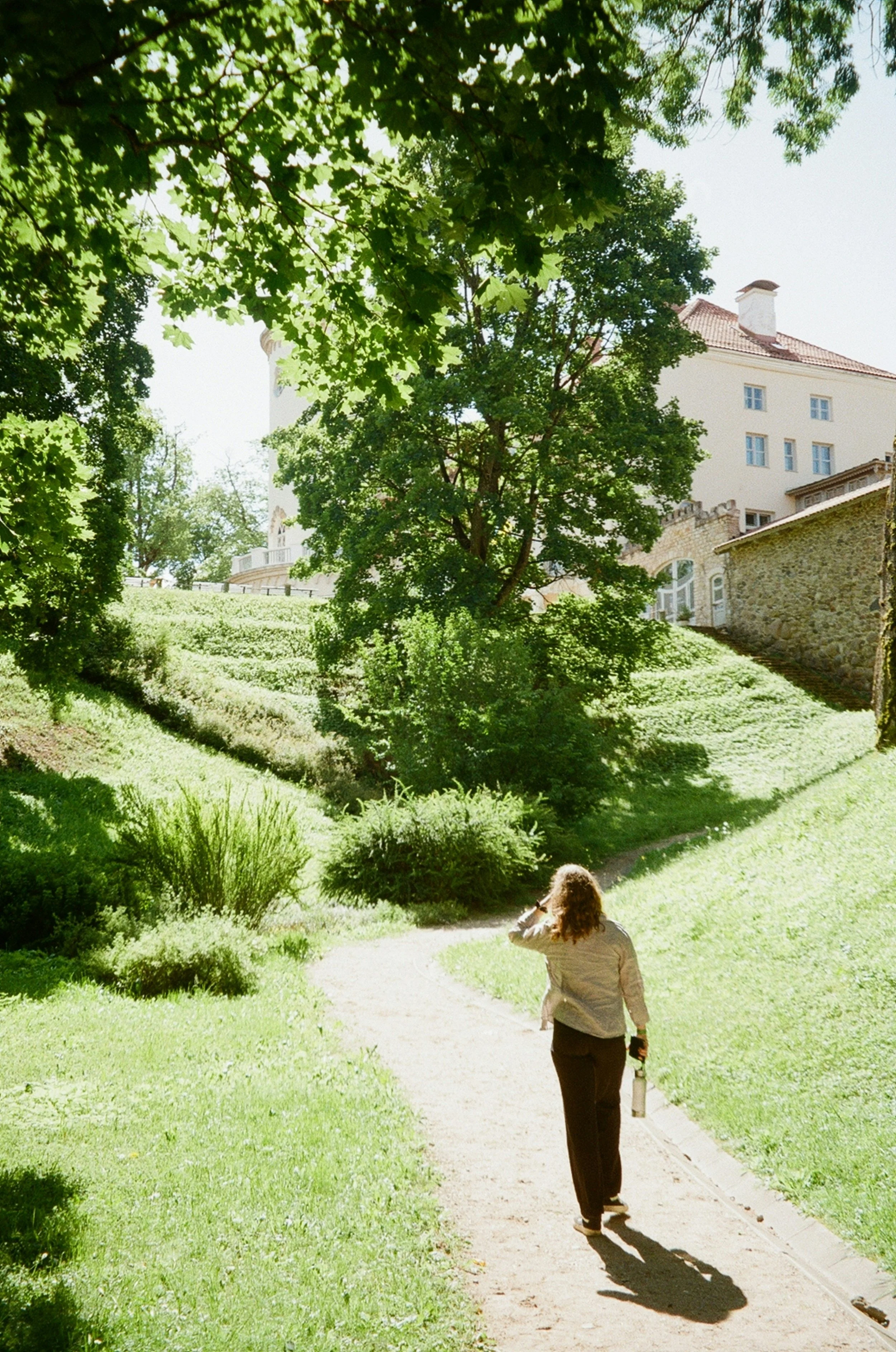 A woman walking along a path through a leafy park.