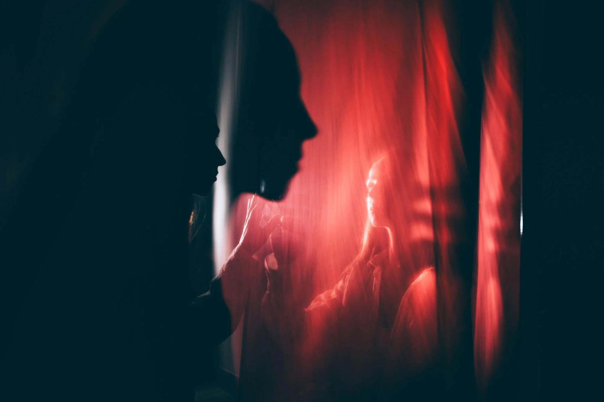 Silhouetted figure facing a softly lit inner self behind a translucent red curtain, symbolizing suppressed anger, inner protection, and a compassionate dialogue between parts of the self.