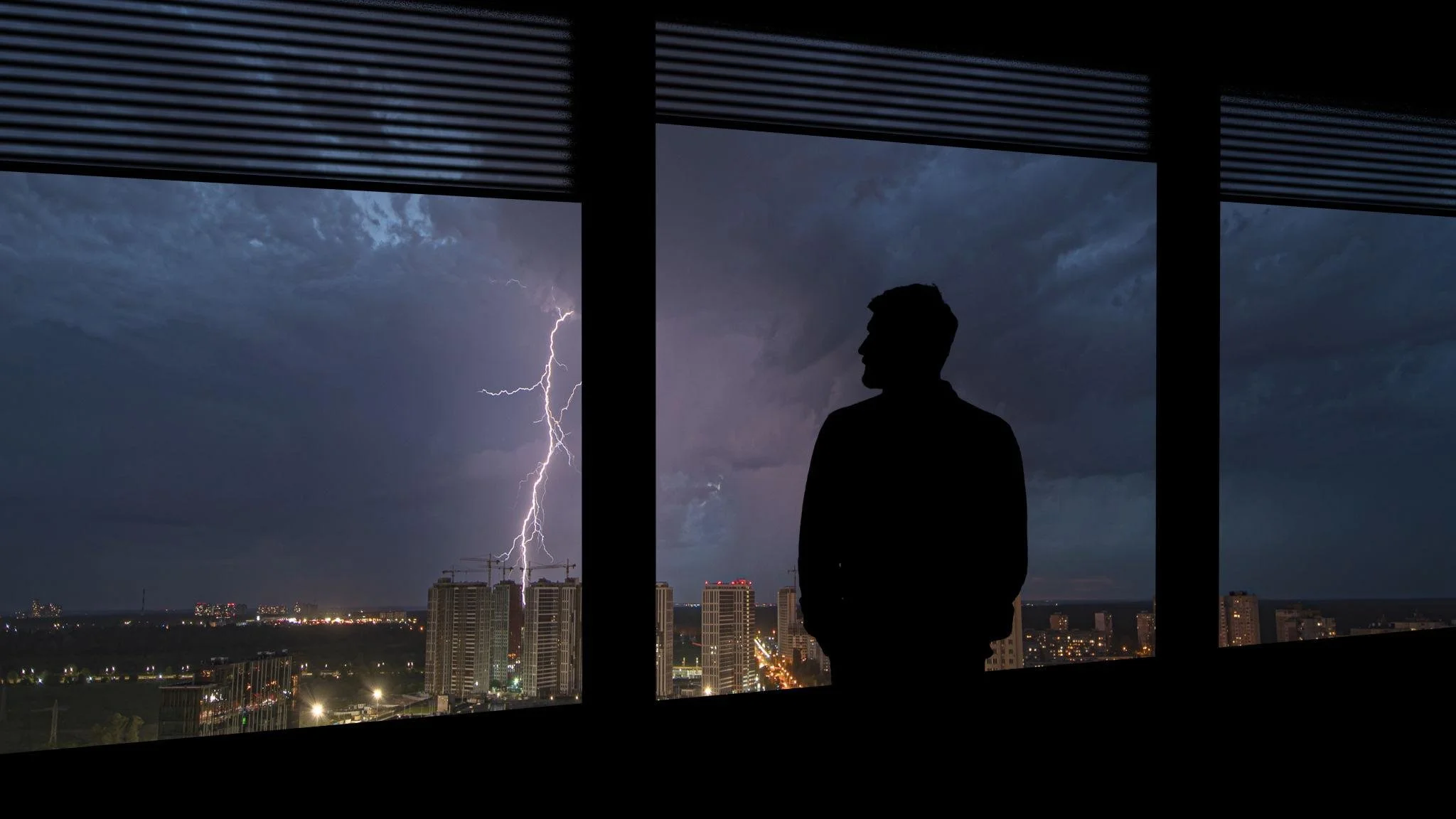 Man standing alone at a high-rise window watching a lightning storm over the city at night -- IFS therapy during divorce
