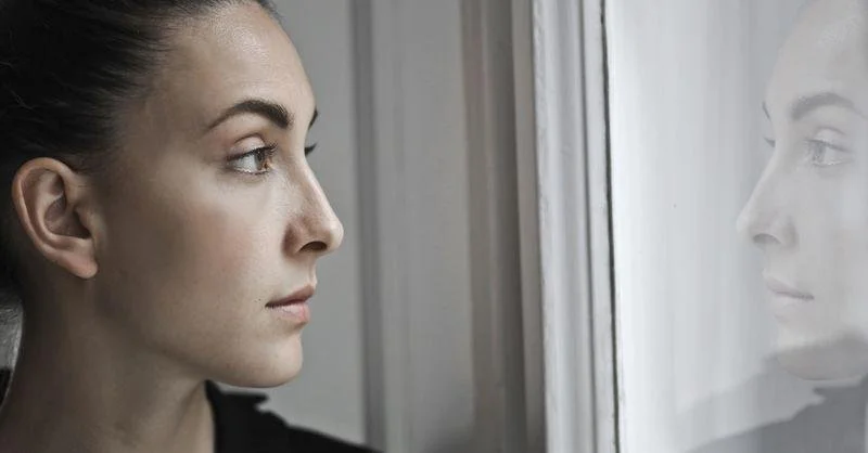 Person gazing thoughtfully at their reflection in a window, symbolising self-awareness and the different inner parts described in Internal Family Systems (IFS).