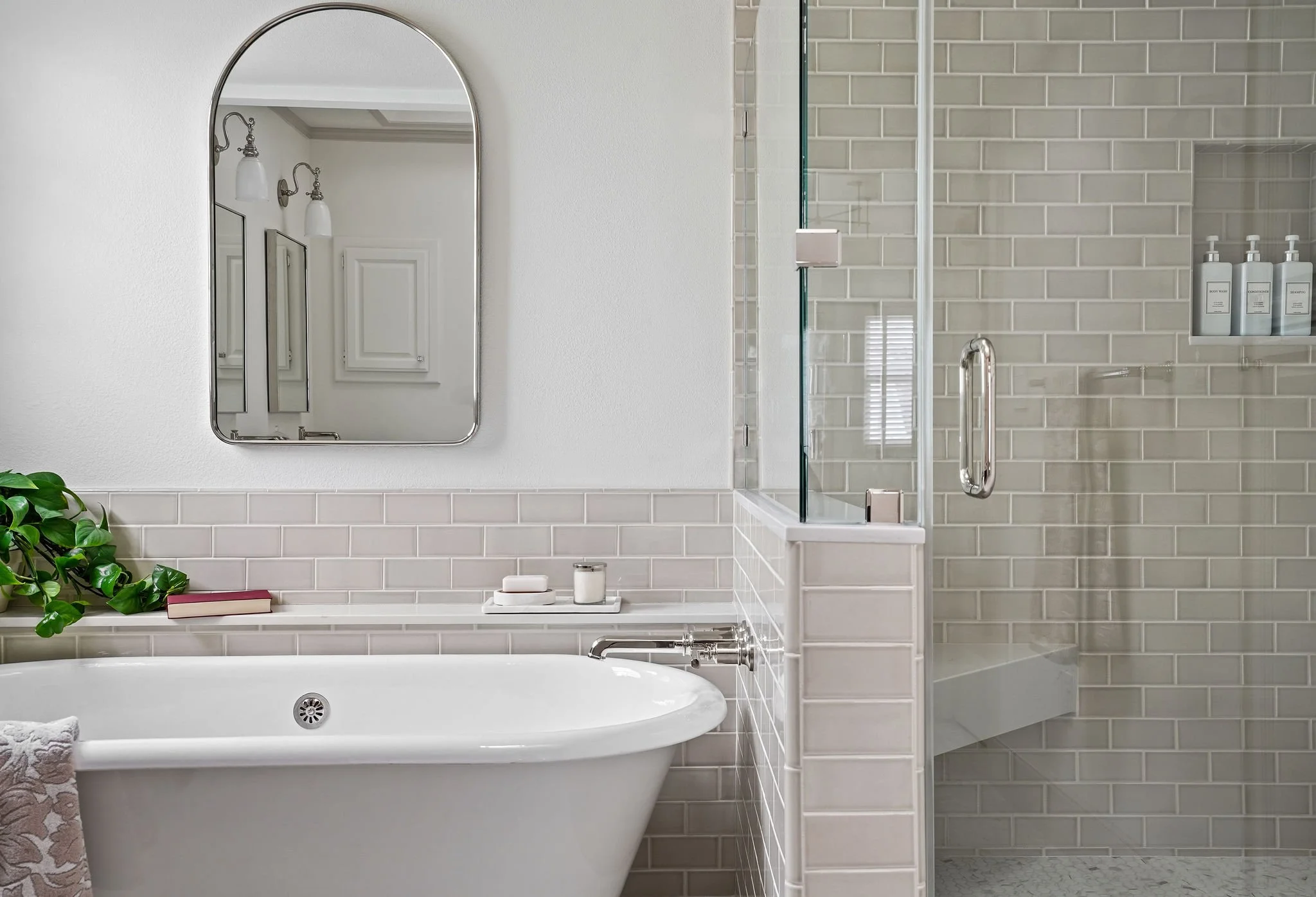 A modern bathroom with a white bathtub, a mirror above, and a shower enclosure with beige subway tiles.