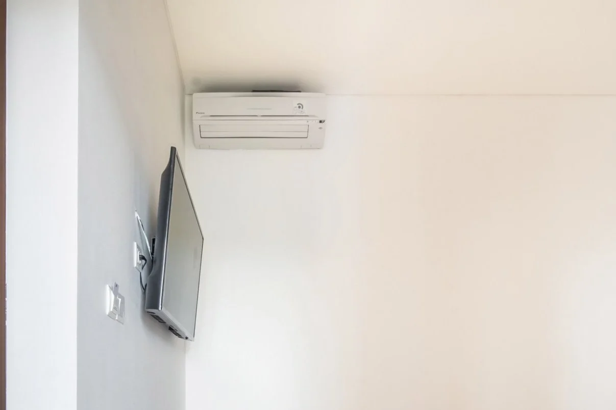 Wall-mounted TV and air conditioner in a room corner.