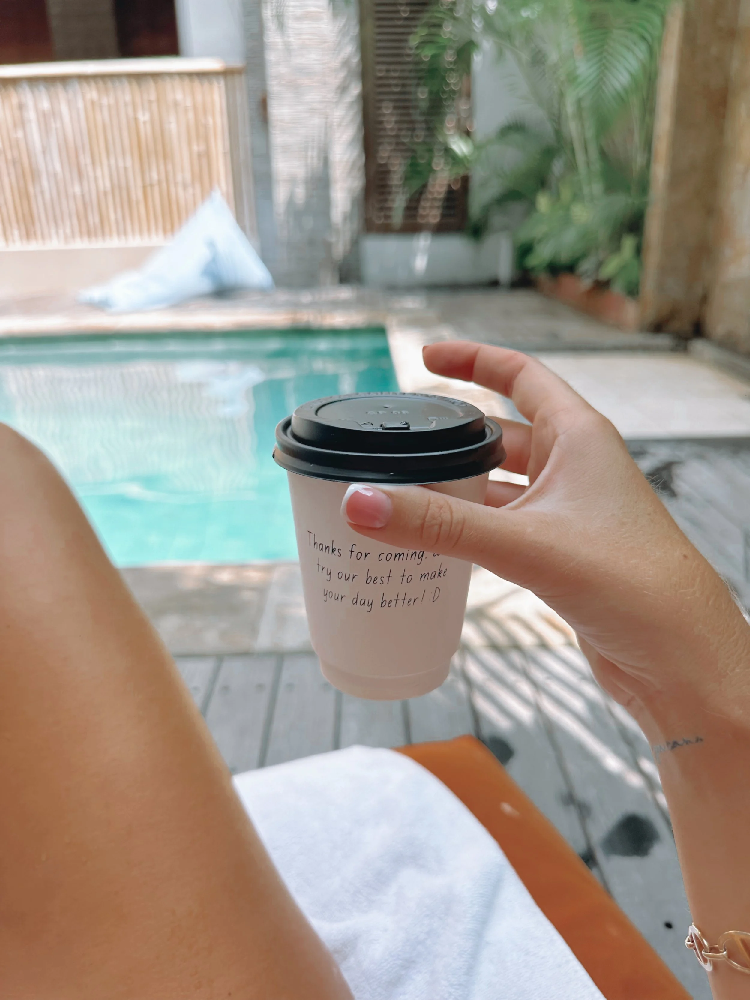 Person holding a coffee cup by a poolside in a tropical setting