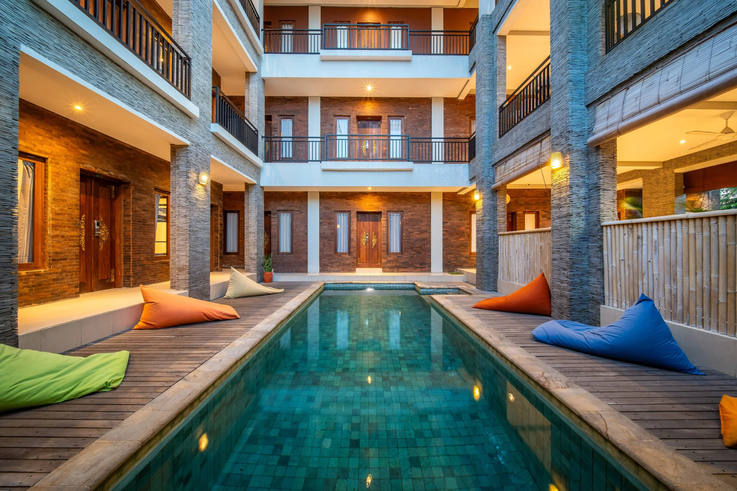 Modern hotel courtyard with swimming pool, lounge chairs, and balconies.