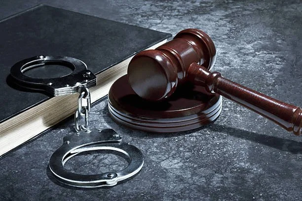 A judge's gavel, a set of handcuffs, and a legal book on a dark surface.