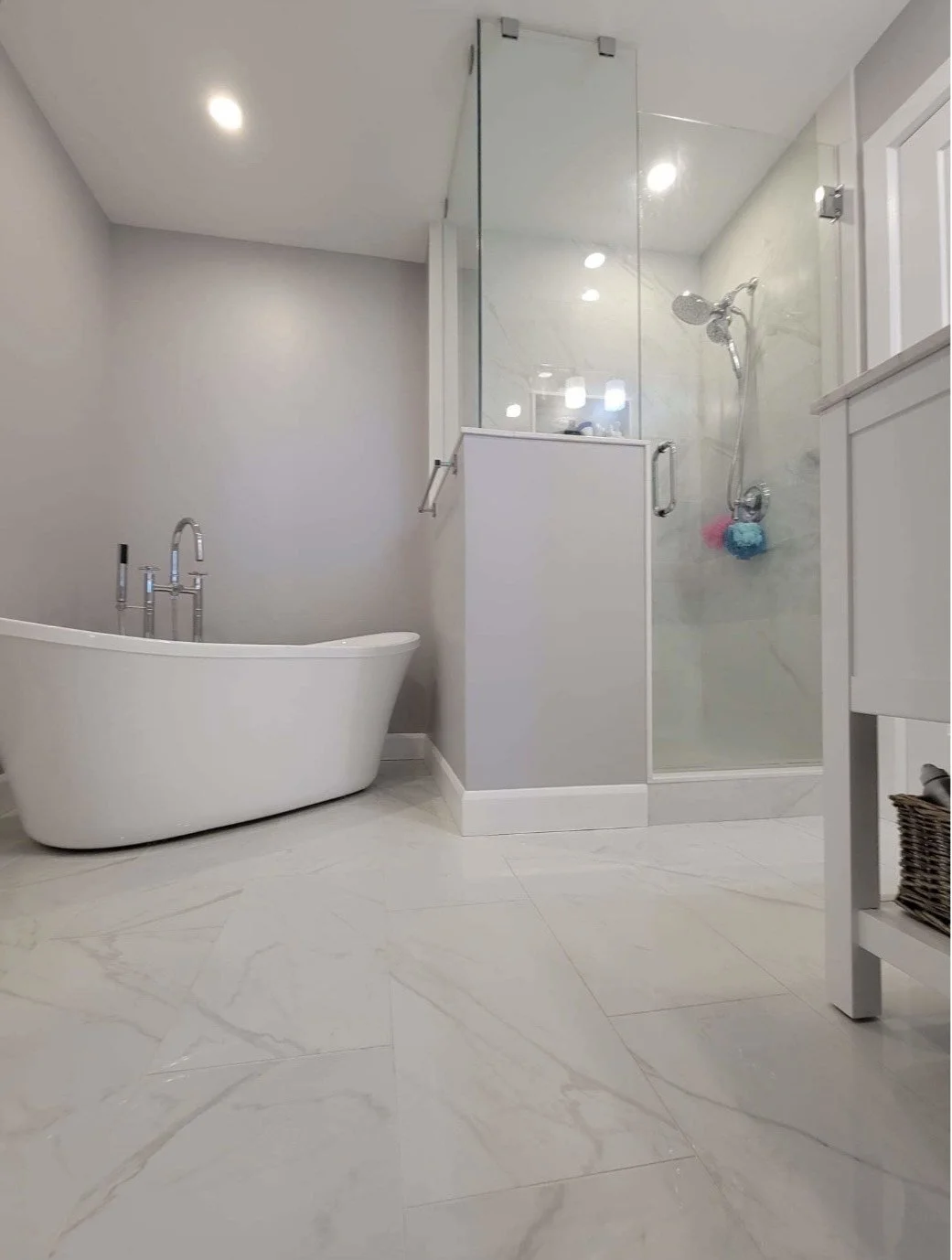 Modern bathroom with a white freestanding bathtub and a glass-enclosed shower area with marble walls and a handheld showerhead.
