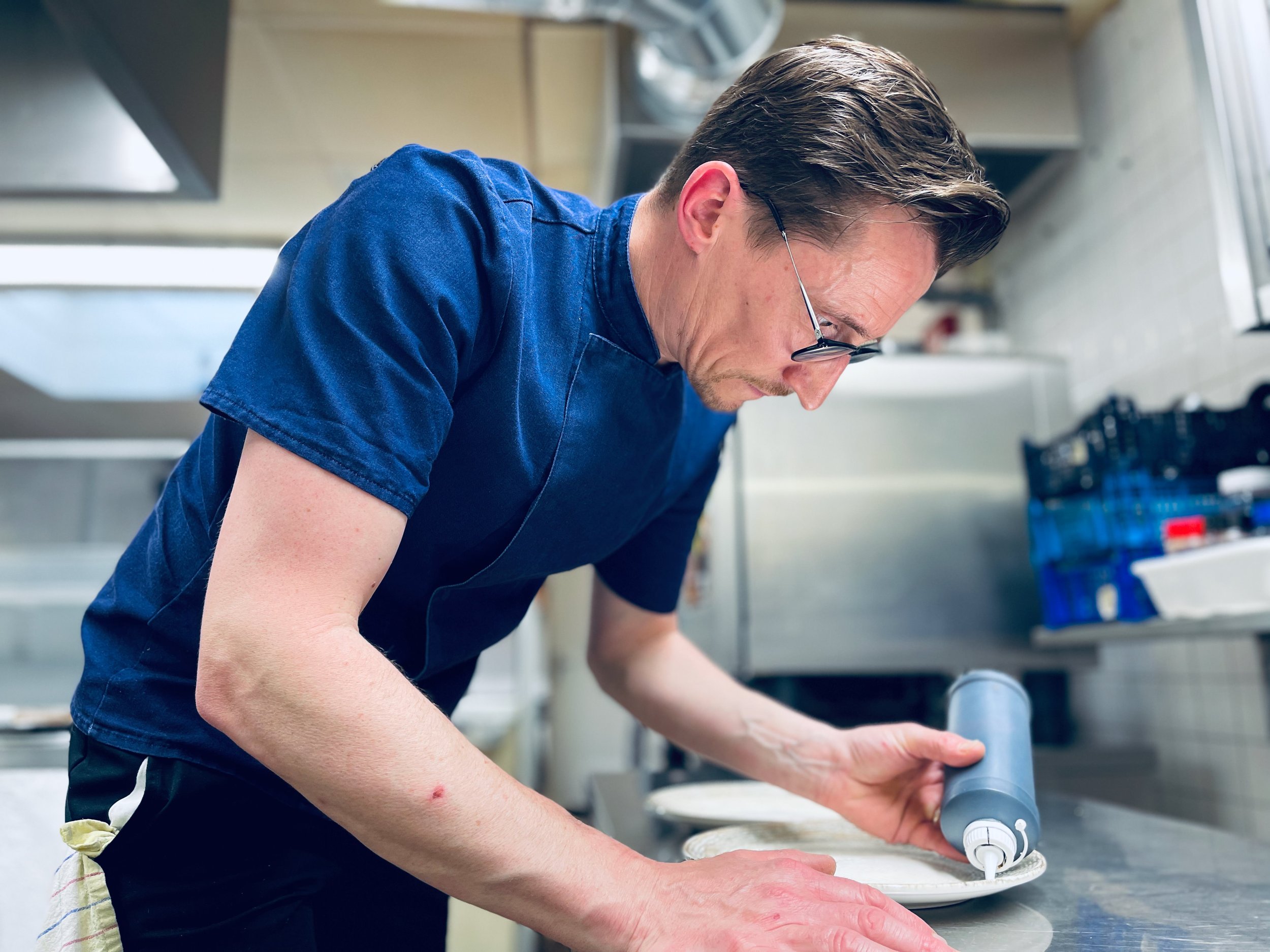 Un chef en cuisine utilisant une bouteille de sauce pour décorer une assiette.