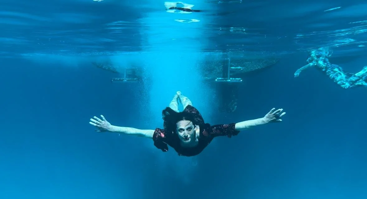 Frau schwimmt unter Wasser mit ausgebreiteten Armen, in der Nähe eines Bootes.