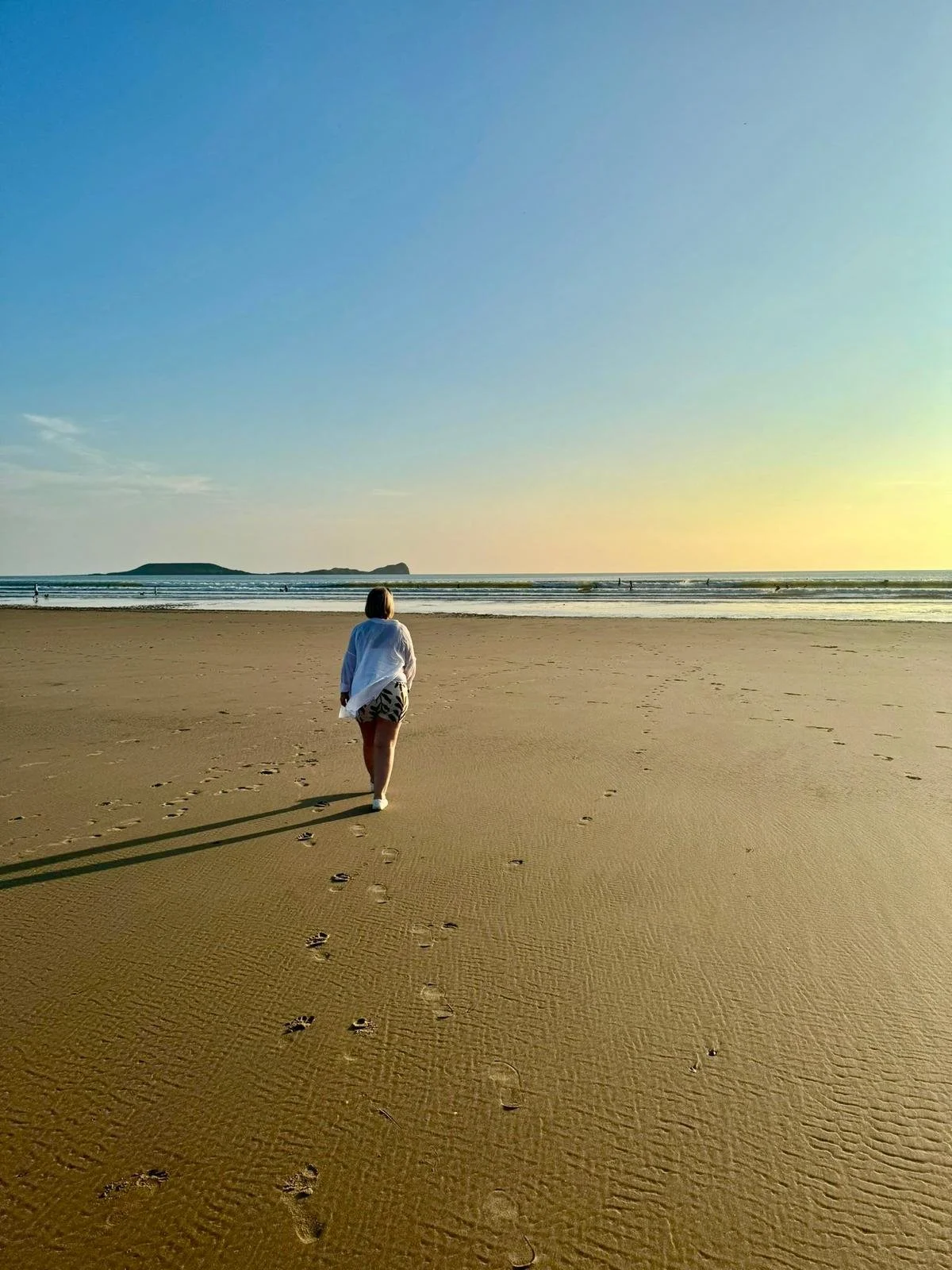 Person walking on a sandy beach towards the ocean during sunset.