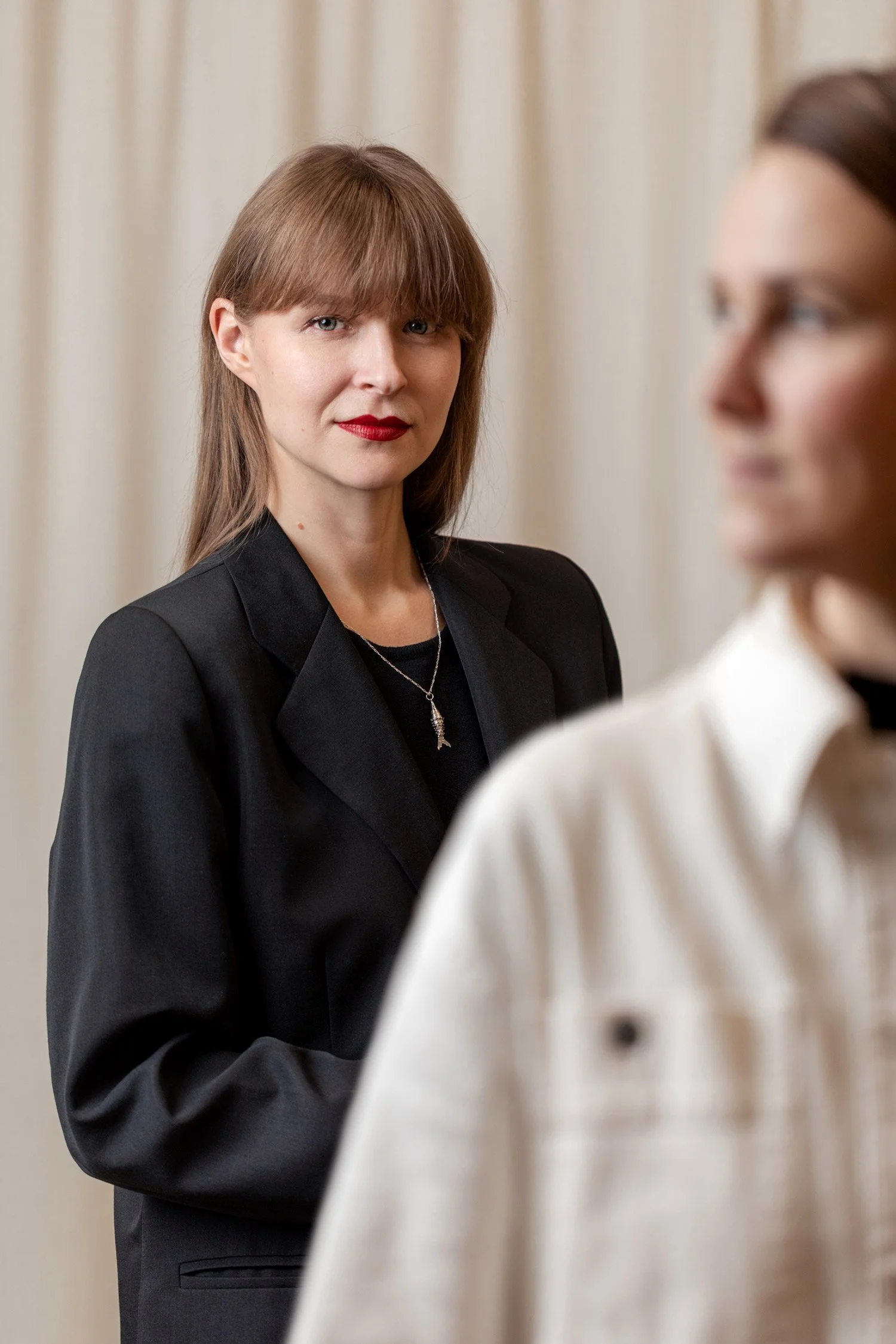 Valokuvaaja Emmi Hyyppä katsoo kameraan ja etualalla sumennetusti visuaalinen suunnittelija Anu Salo