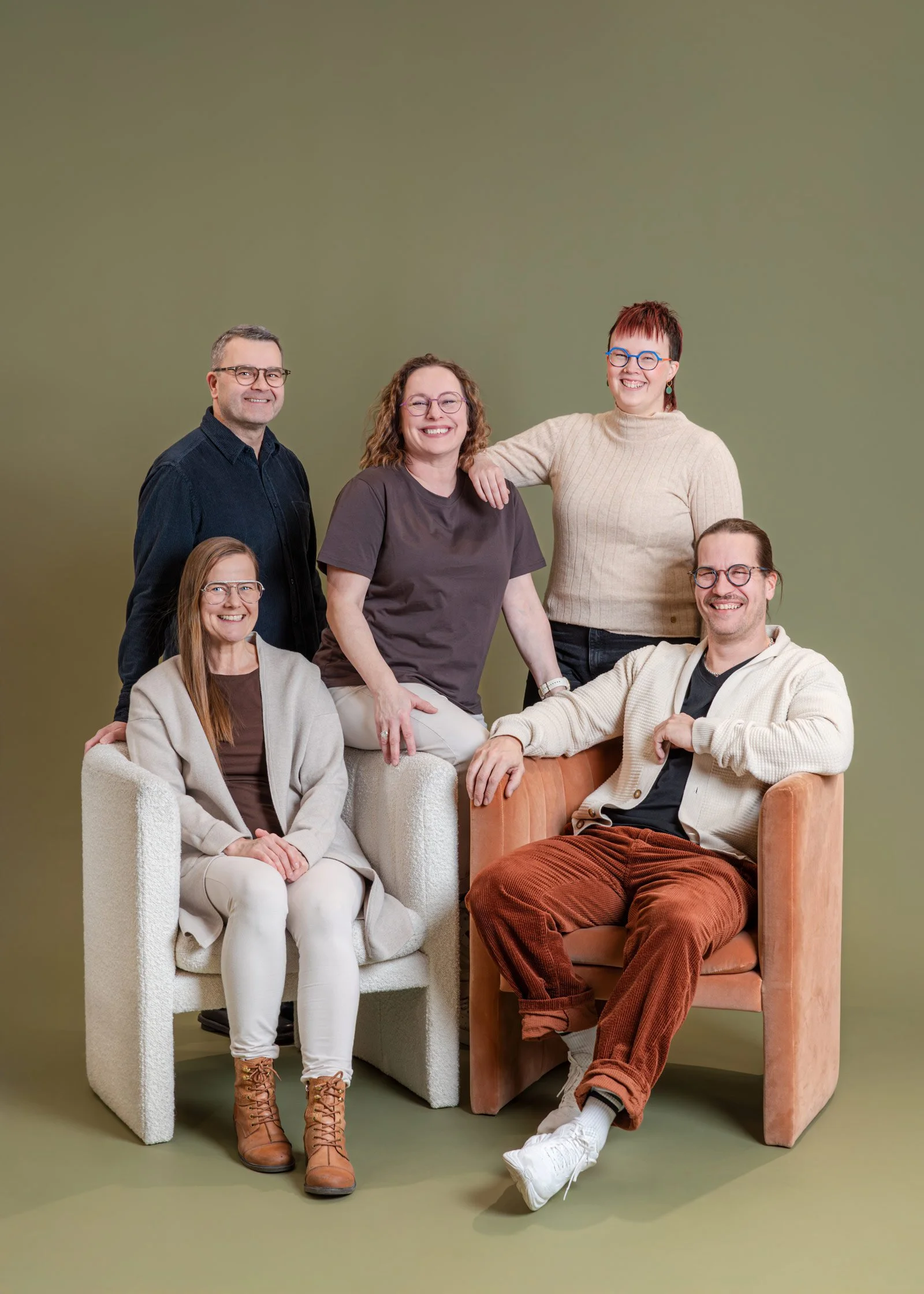 Optikkoliikkeen henkilökunta iloisessa ryhmäkuvassa murretun vihreää taustakangasta vasten