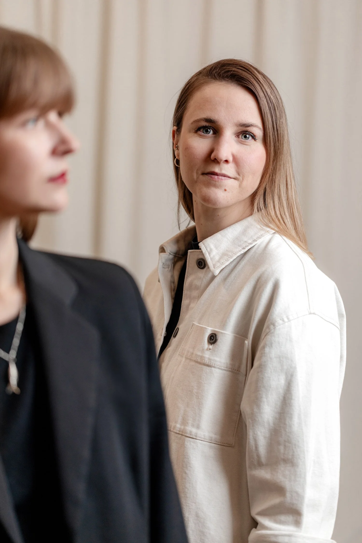 Etualalla sumennetusti valokuvaaja Emmi Hyyppä ja visuaalinen suunnittelija Anu Salo katsoo kameraa kohti