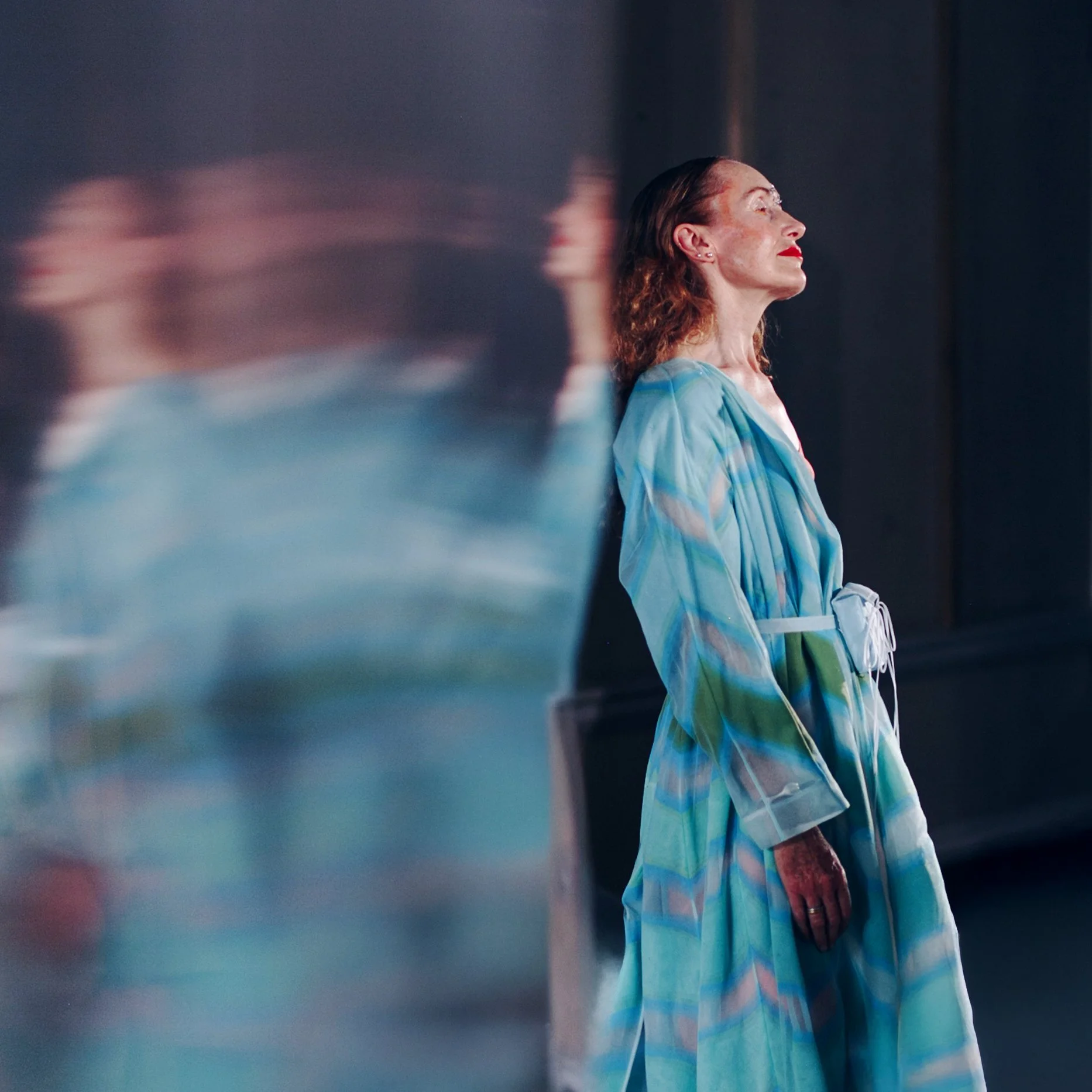 Sinimekkoinen nainen nojailee heijastavalle pinnalle ja pitää silmiään kiinni.