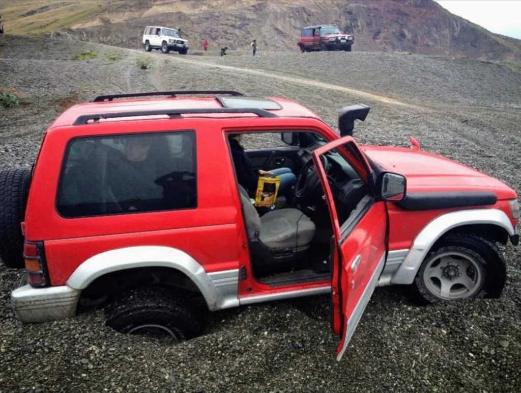 Red Mitsubishi Pajero buried to the frame in deep volcanic scree during an off-road recovery situation.