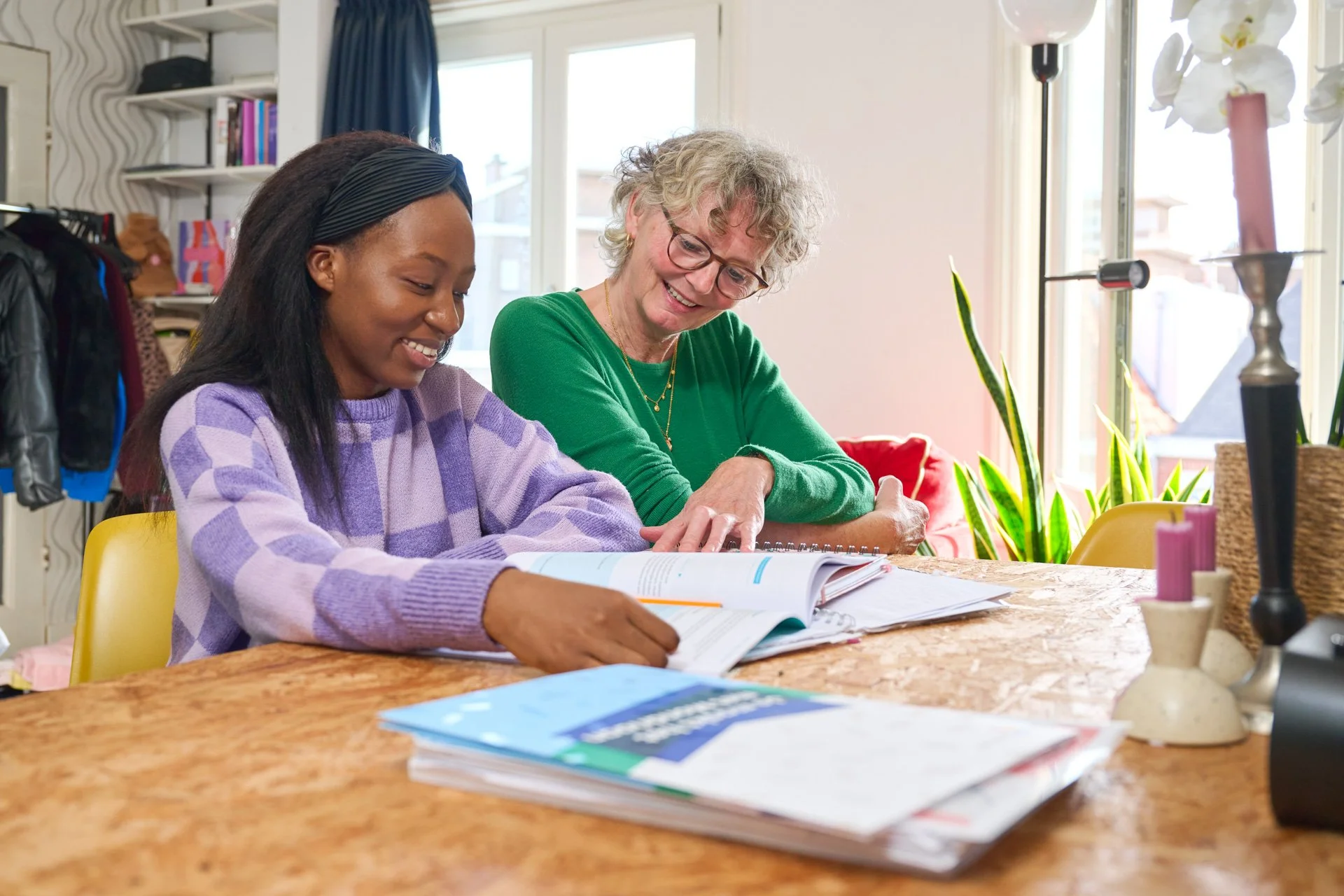 Jonge zwarte vrouw is aan het studeren. Een oudere vrouw helpt haar en kijkt mee. 