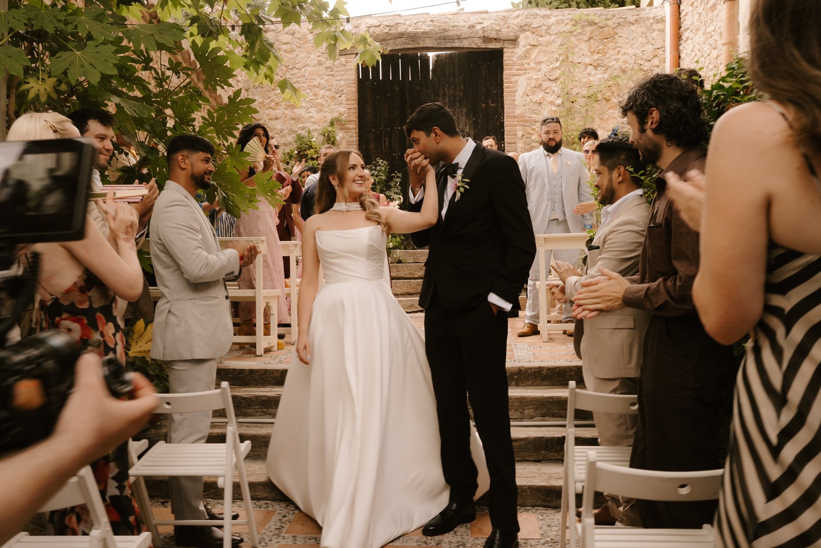 Groom kisses bride's hand during the recessional at Mediterranean wedding