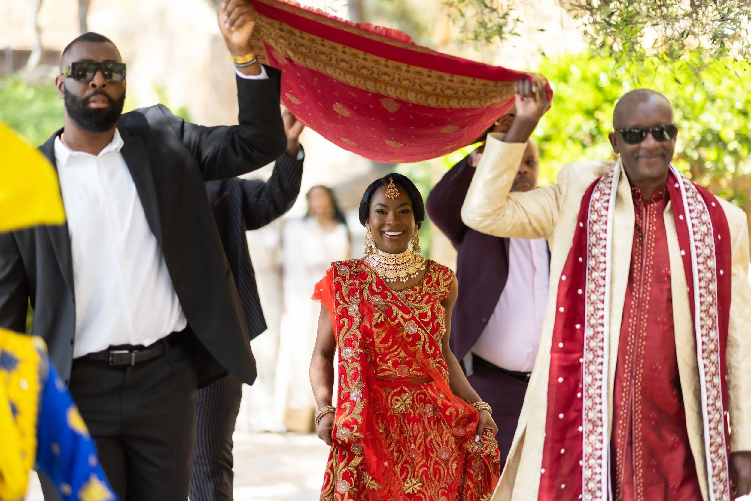 Bride walking towards the ceremony beneath a traditional ceremonial cloth.