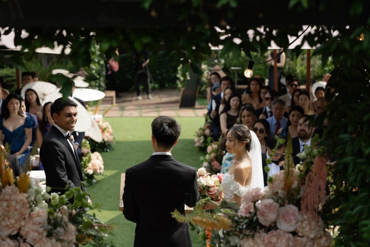 Wedding couple during ceremony surrounded by florals and guests.
