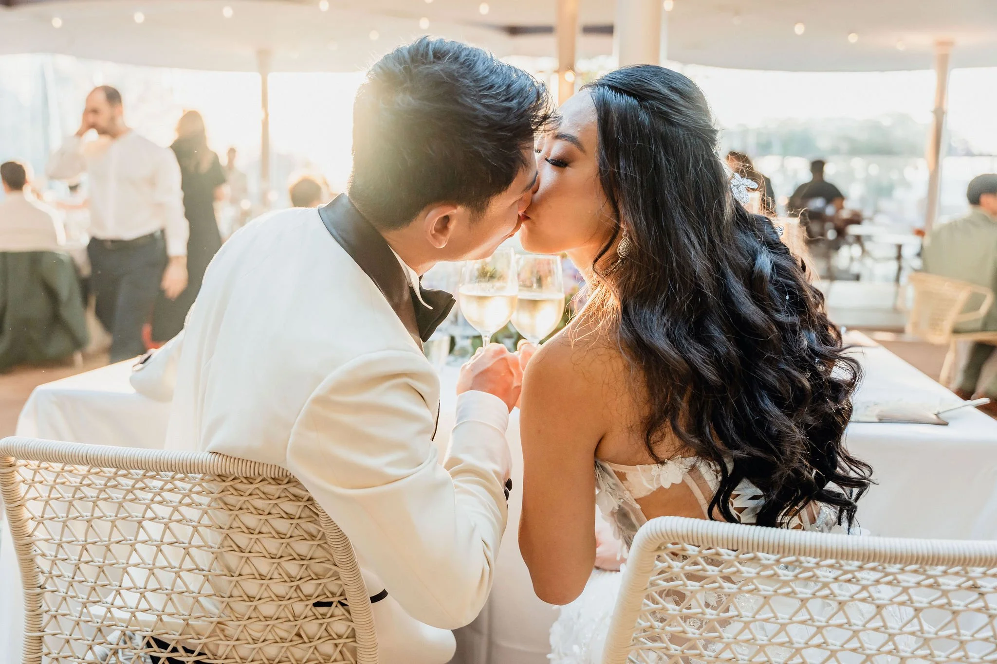 Newlyweds kissing at their banquet table with glasses of champagne in warm sunset light, October wedding