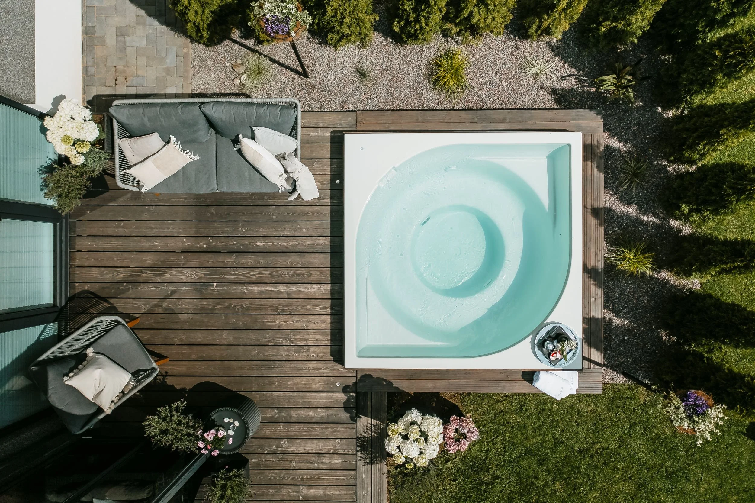 Ülaltvaade puidust terrassile, kus on loodud puhkeala integreeritud terrassivanni, diivani, aiatoolide ja lilledega.