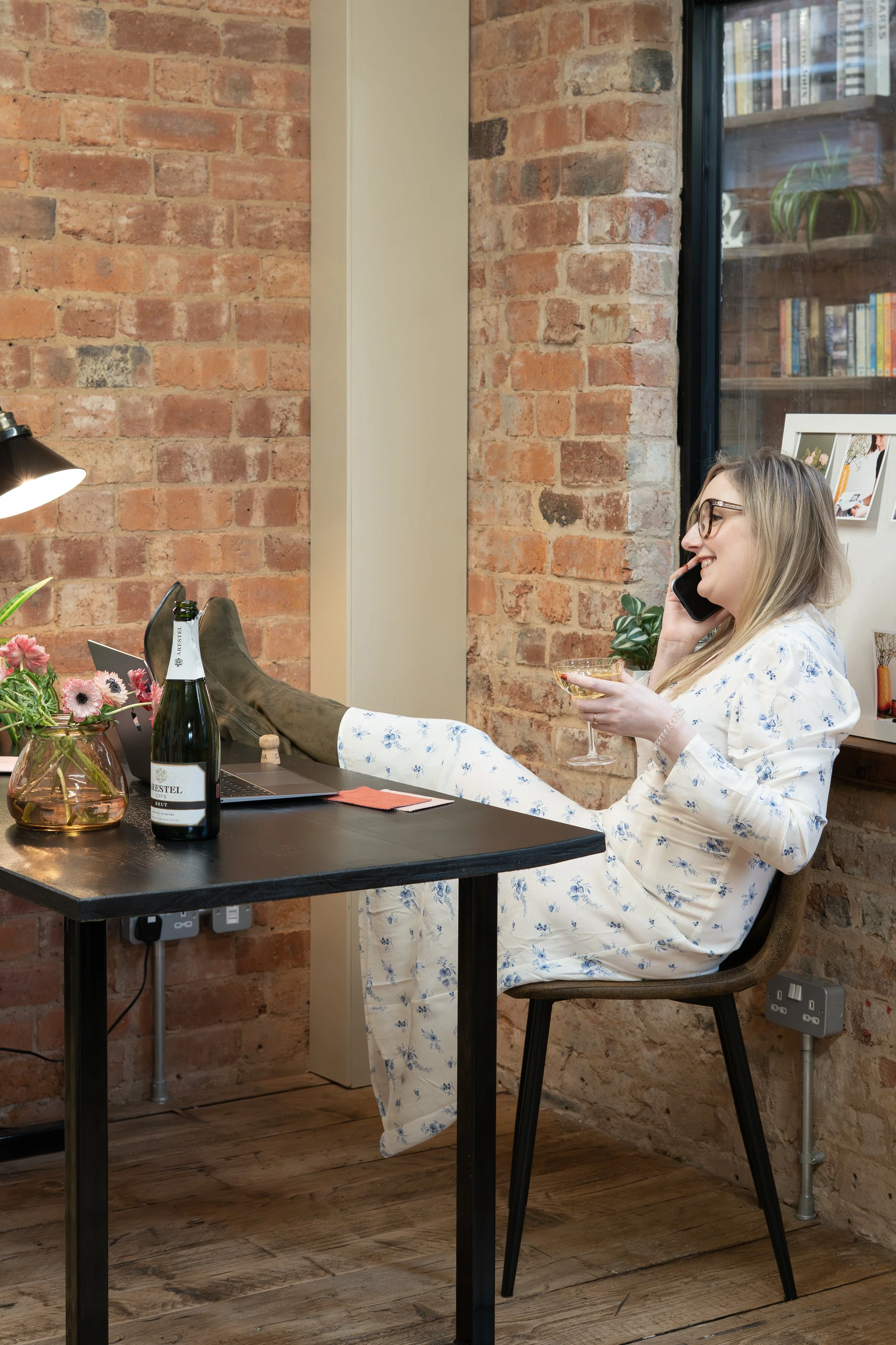 Wedding and SEO expert Zoe Burke sits at her desk with her feet up sipping champagne on a phone call