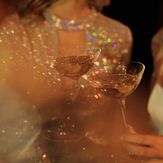 A blurry stylistic image of a bride in a sparkly dress with a glass of champagne