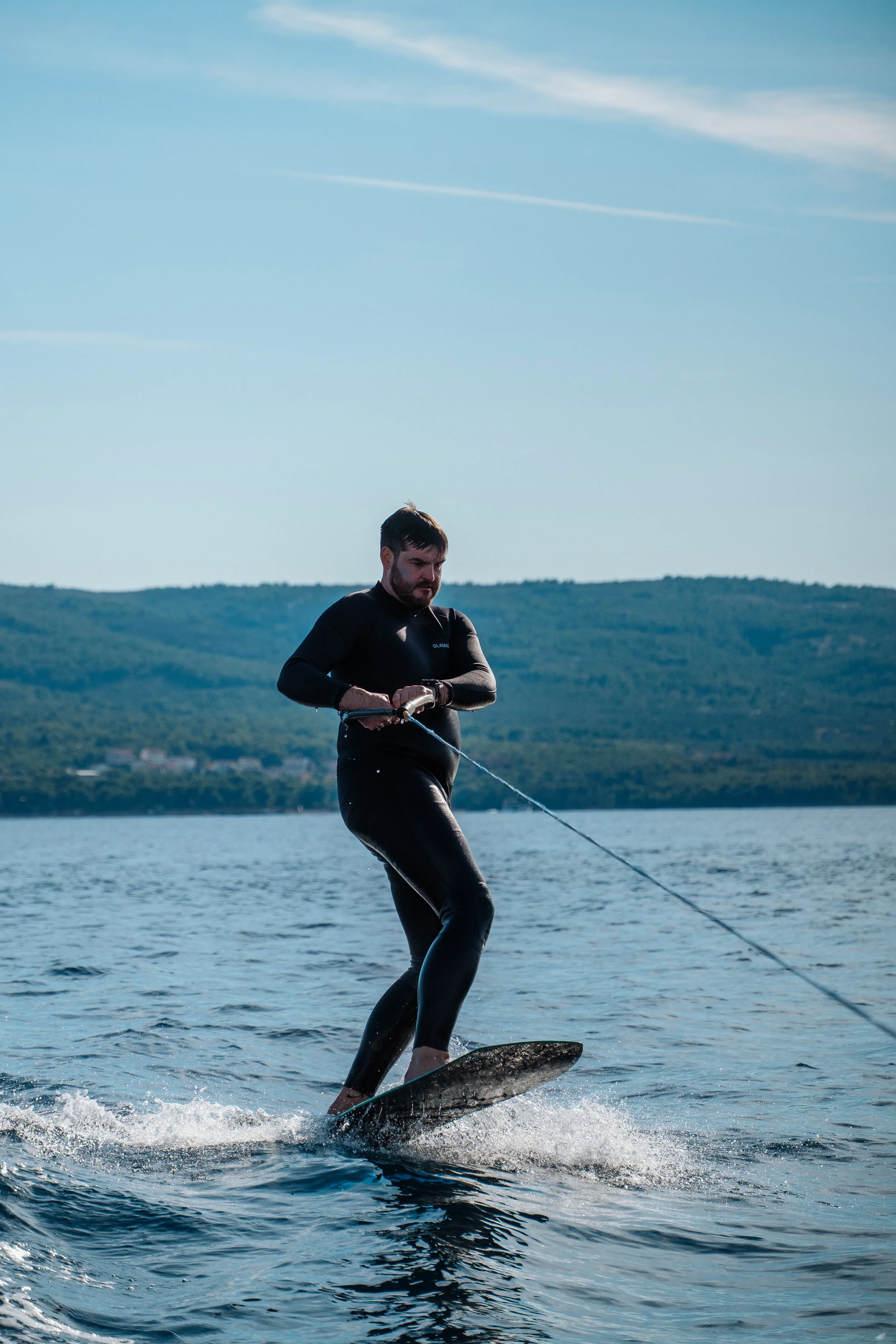 Man wakeboarding on a lake with a backdrop of green hills under a blue sky.