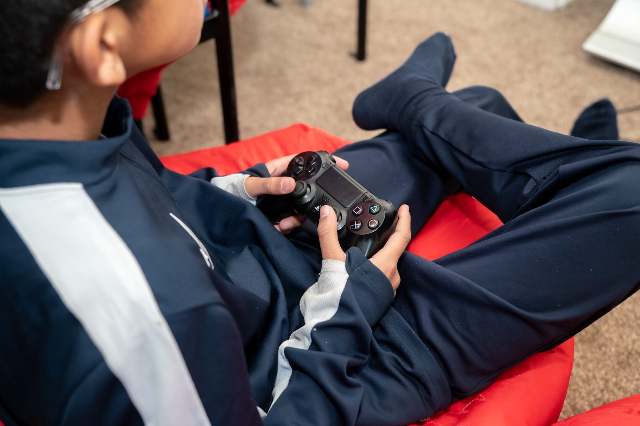 Person sitting on a red bean bag holding a black gaming controller.