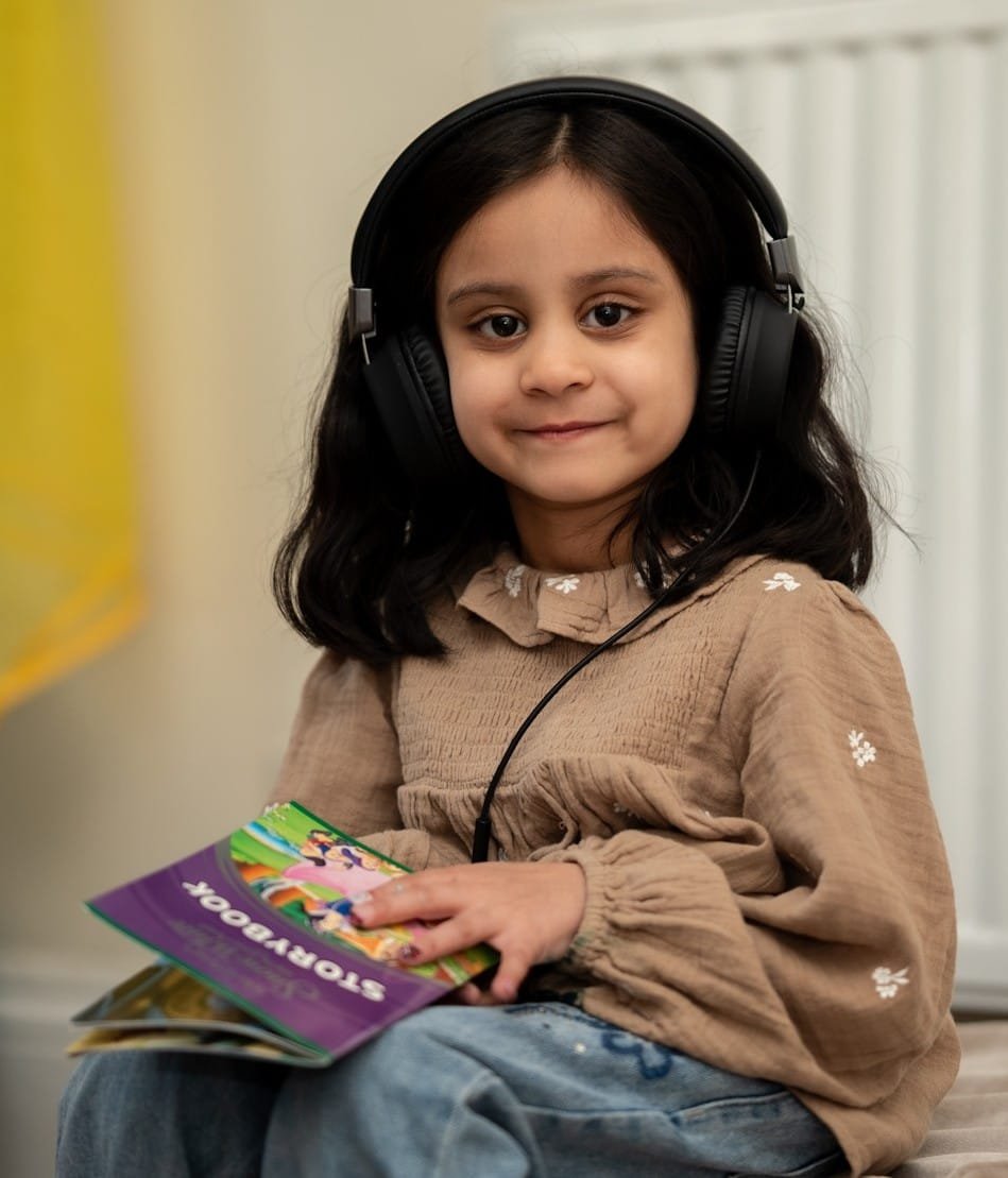 Child with headphones holding a storybook