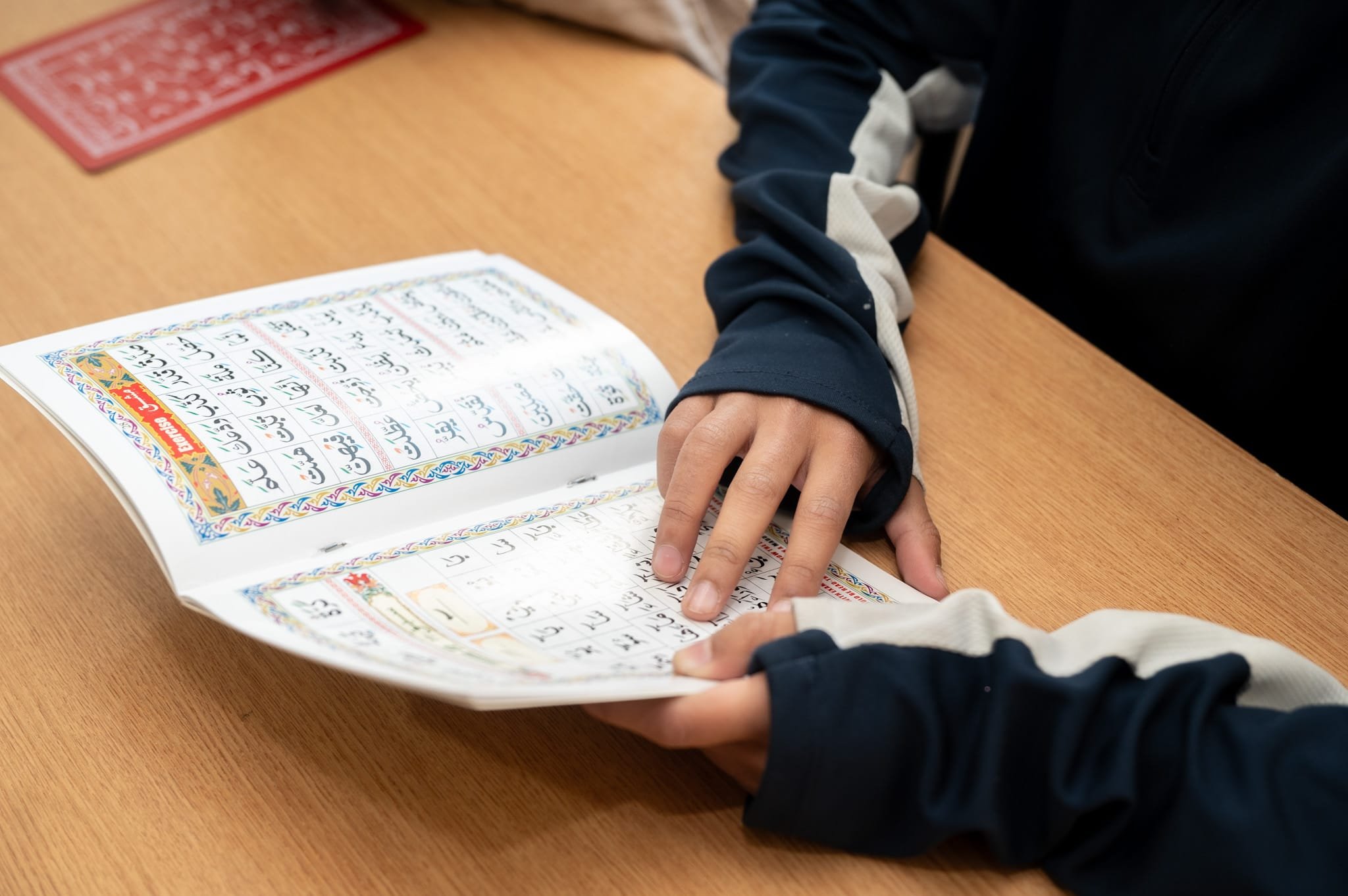 Person reading a book in Arabic script on a wooden table.