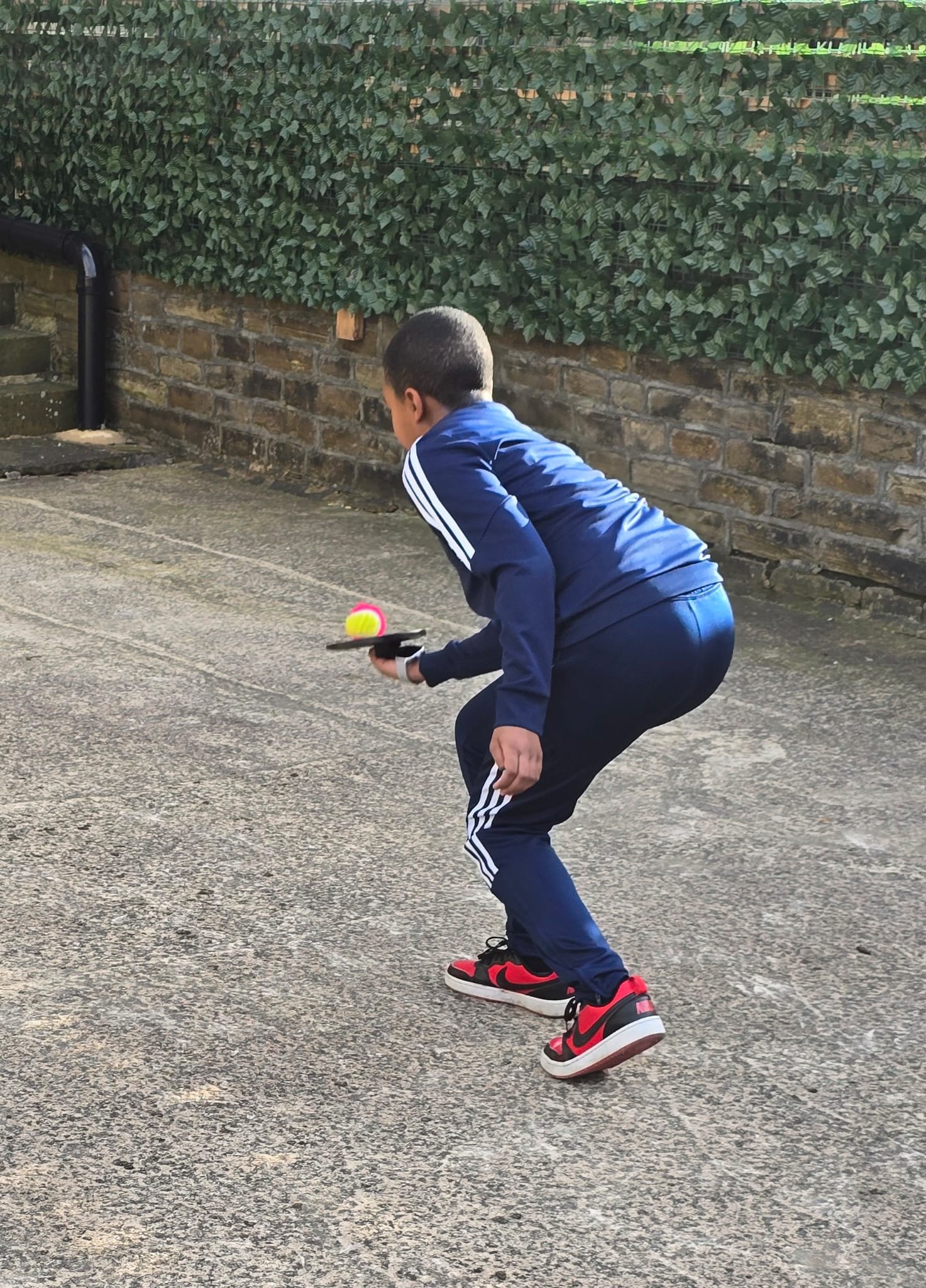 Young boy in tracksuit playing with a paddle ball outdoors.