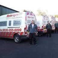 Four people standing next to several Mobi-tire service vans parked outdoors.
