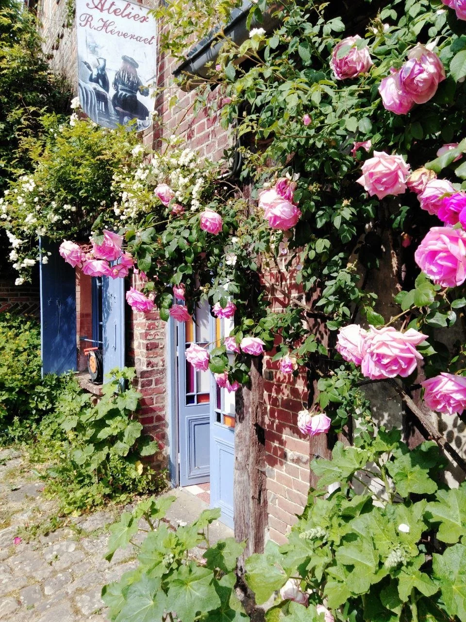 Un artiste peint un paysage de verger avec des arbres en fleurs, tenant une palette de peinture. Le tableau est posé sur un chevalet à côté d'une fenêtre.
