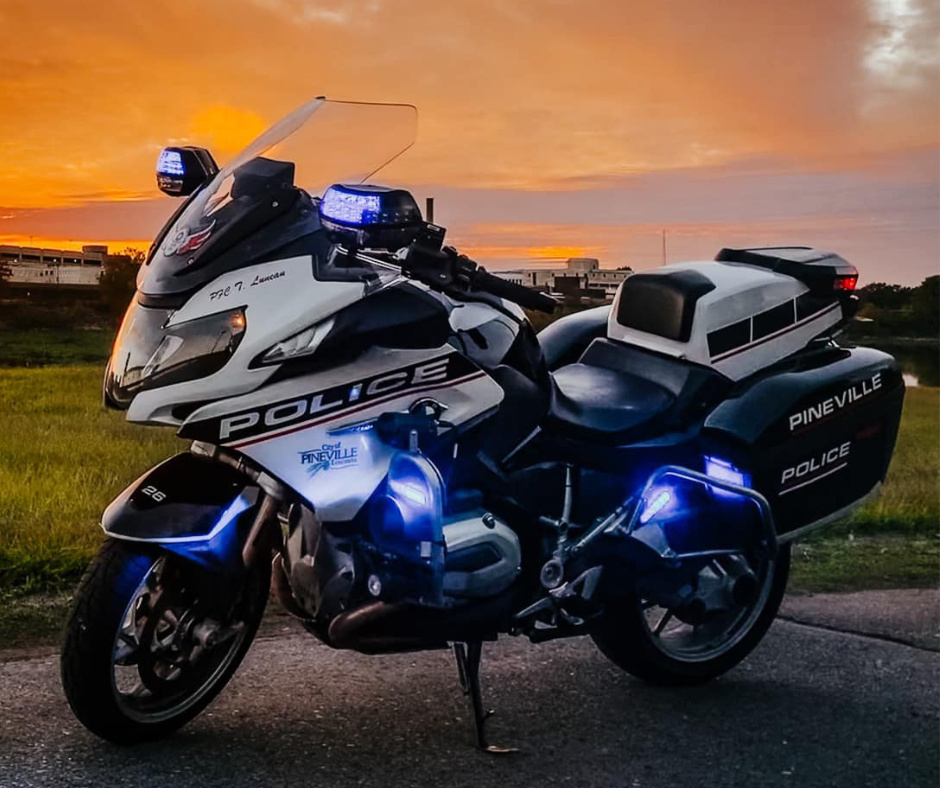 Police motorcycle with blue lights on, parked on a road during sunset.