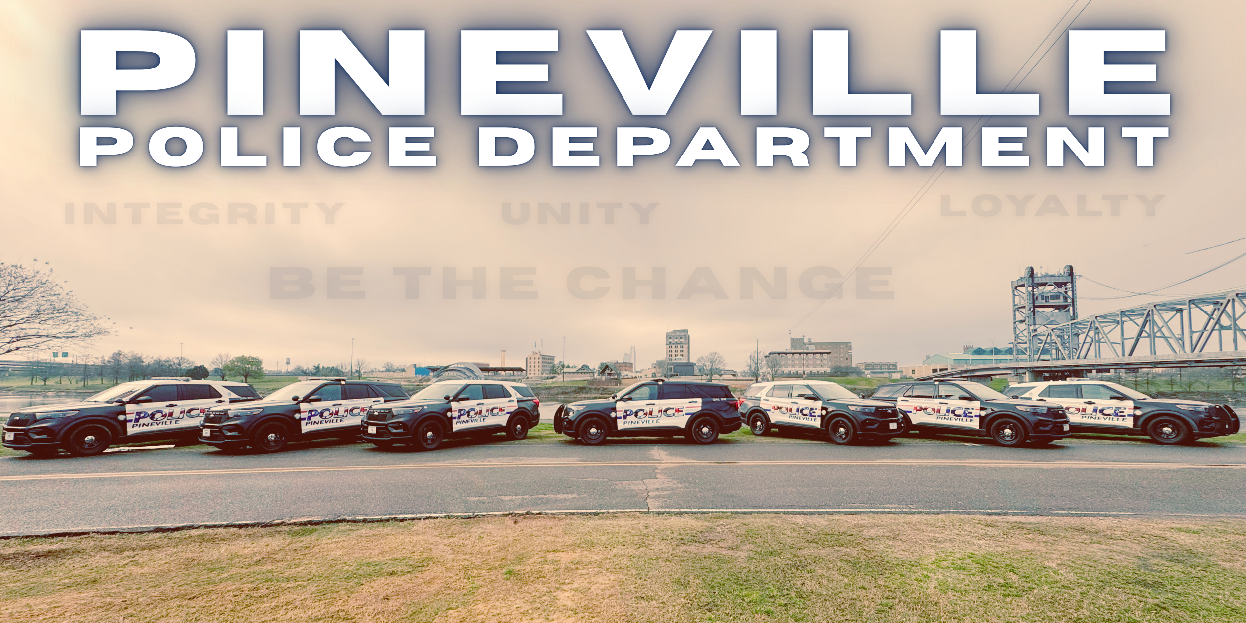 Six police cars parked in a row on a road with a city skyline and bridge in the background, overlaid with the text 'Pineville Police Department' and words like 'Integrity,' 'Unity,' 'Loyalty,' and 'Be the Change'.